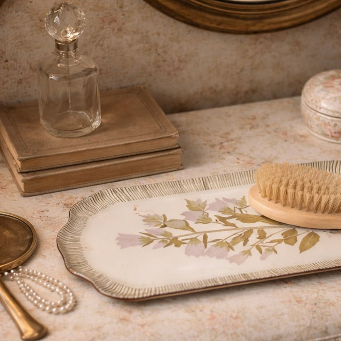Vintage-style vanity setup with a glass decanter, brush, and decorative tray on a textured surface.