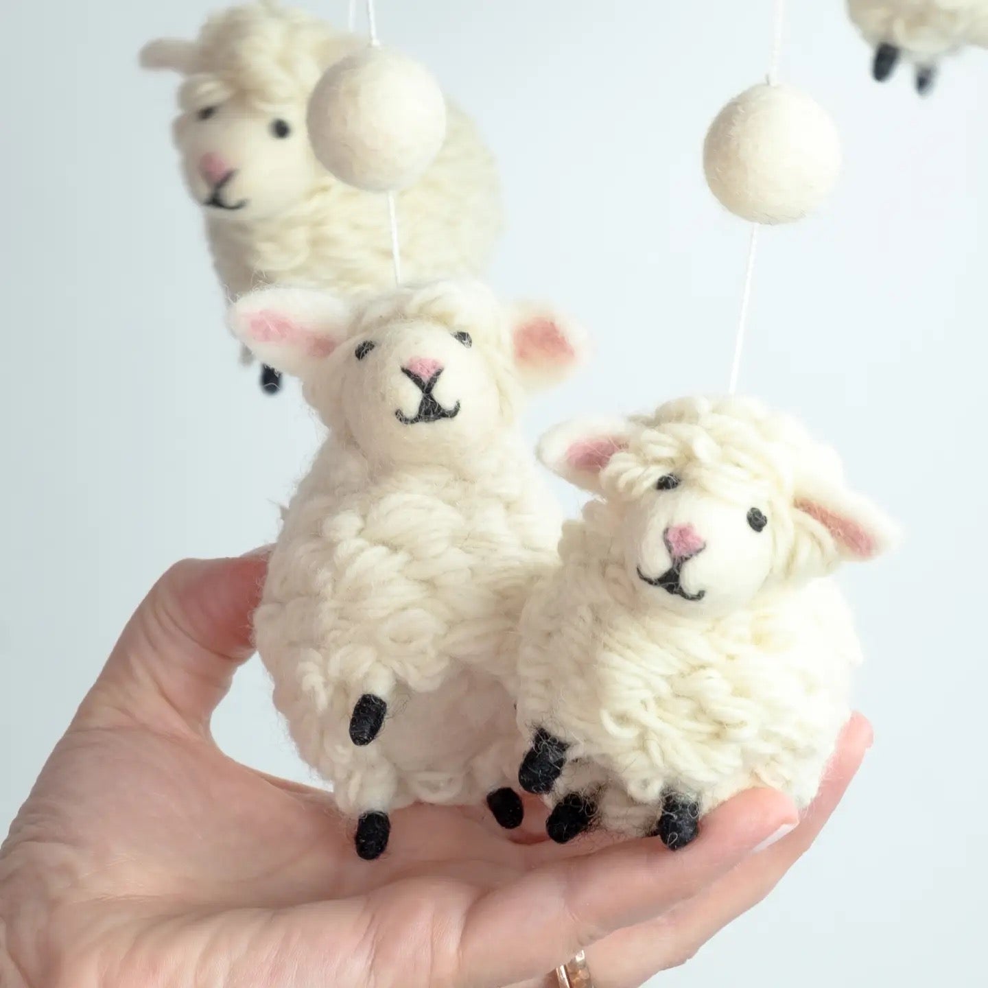 Hand holding three fluffy white sheep toys against a light background