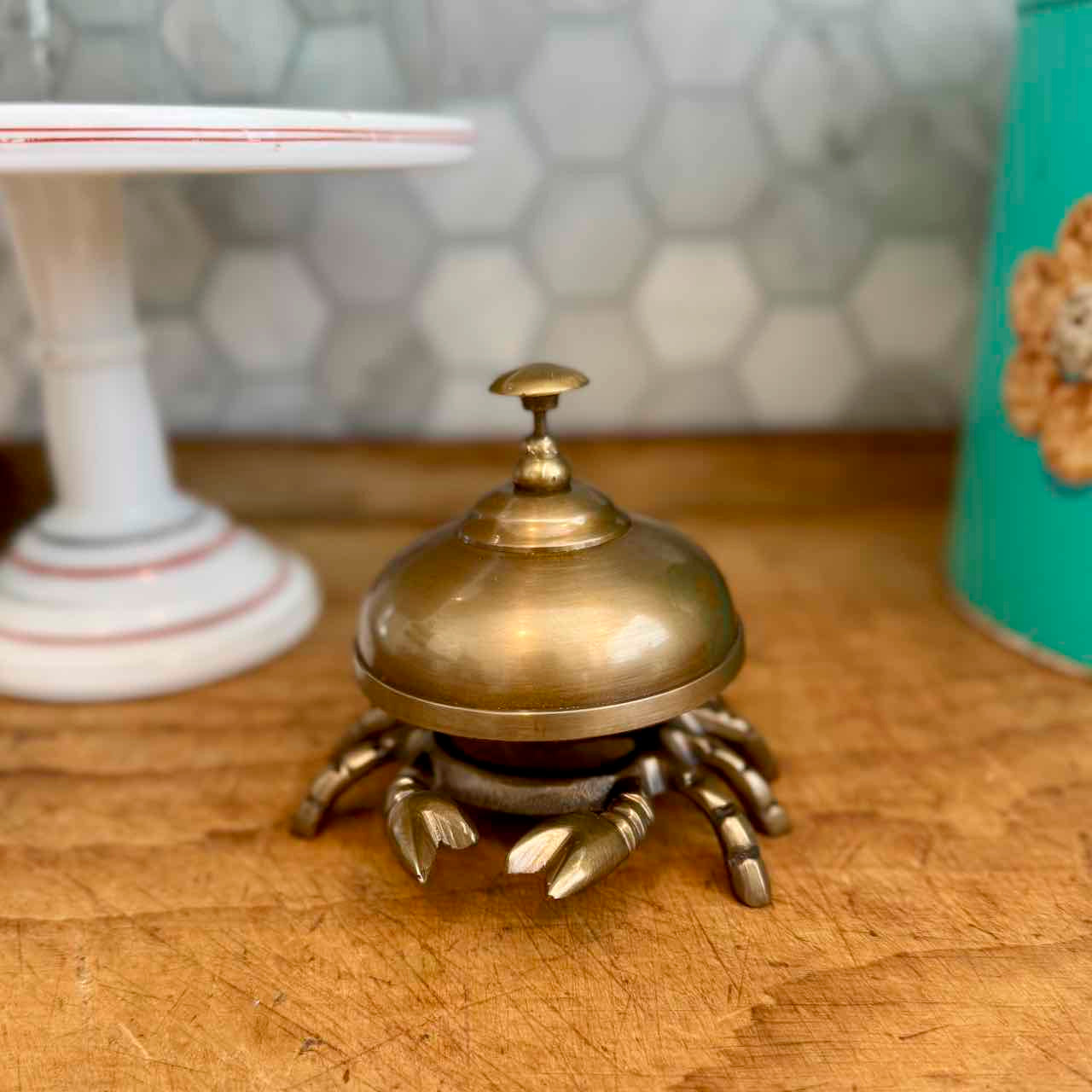 A brass lobster-shaped bell ringer with a domed lid and eight claw-like feet, resting on a wooden tabletop with a blurred background.