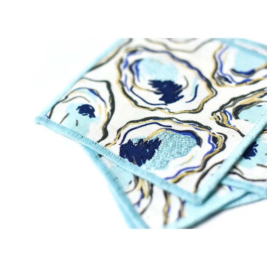 Two square coasters with oyster shell design on a light blue background