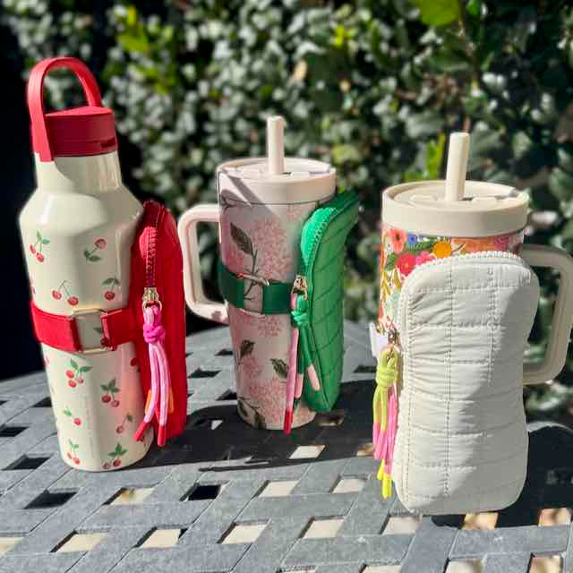 Three insulated drink containers with handles and colorful designs on a table outdoors.