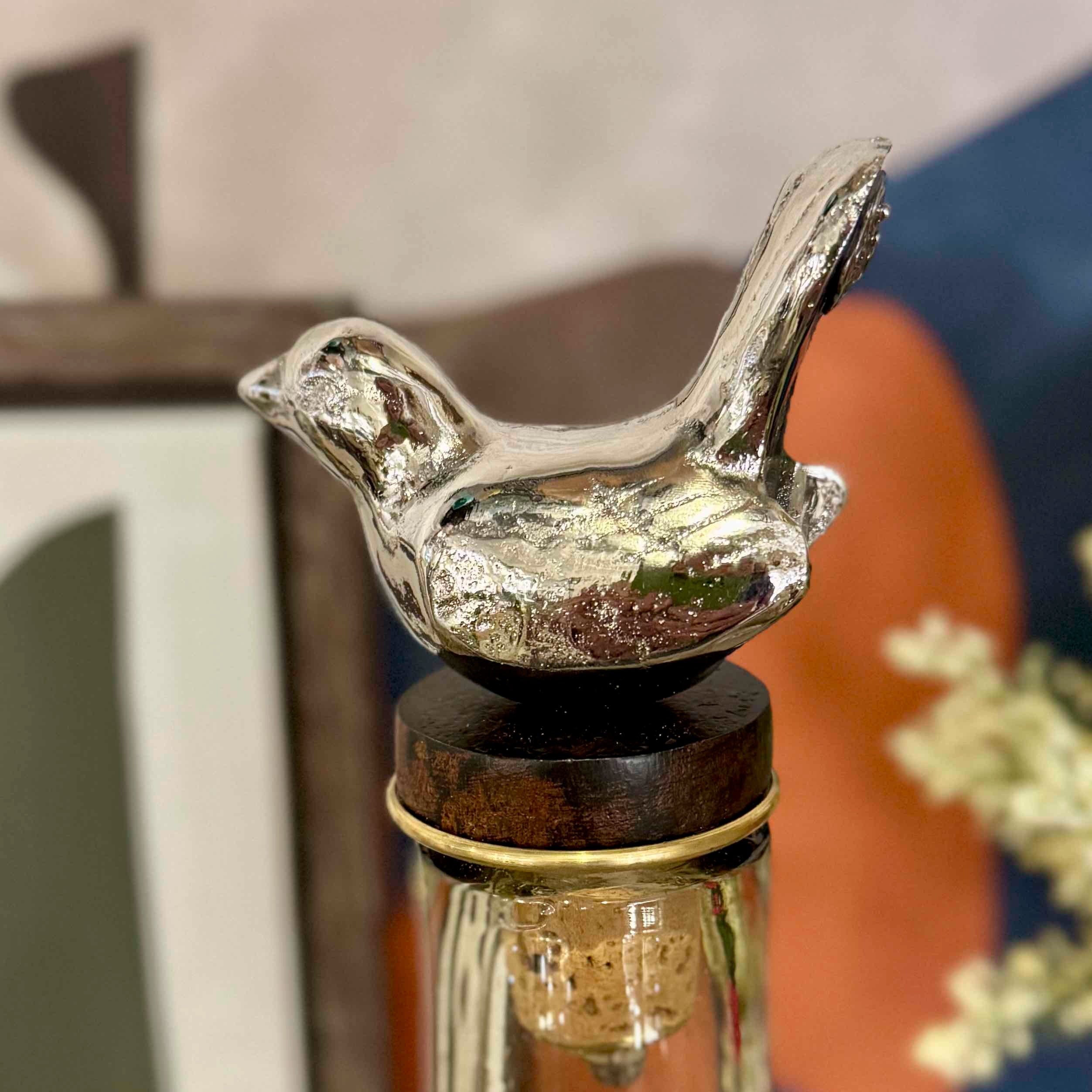 Silver bird-shaped bottle stopper on a wooden base with a blurred background