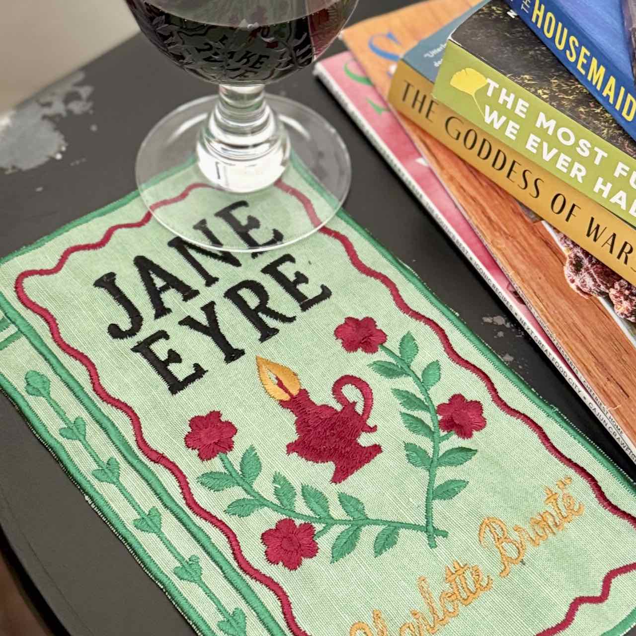 Book cover of 'Jane Eyre' with a glass of wine and books in the background