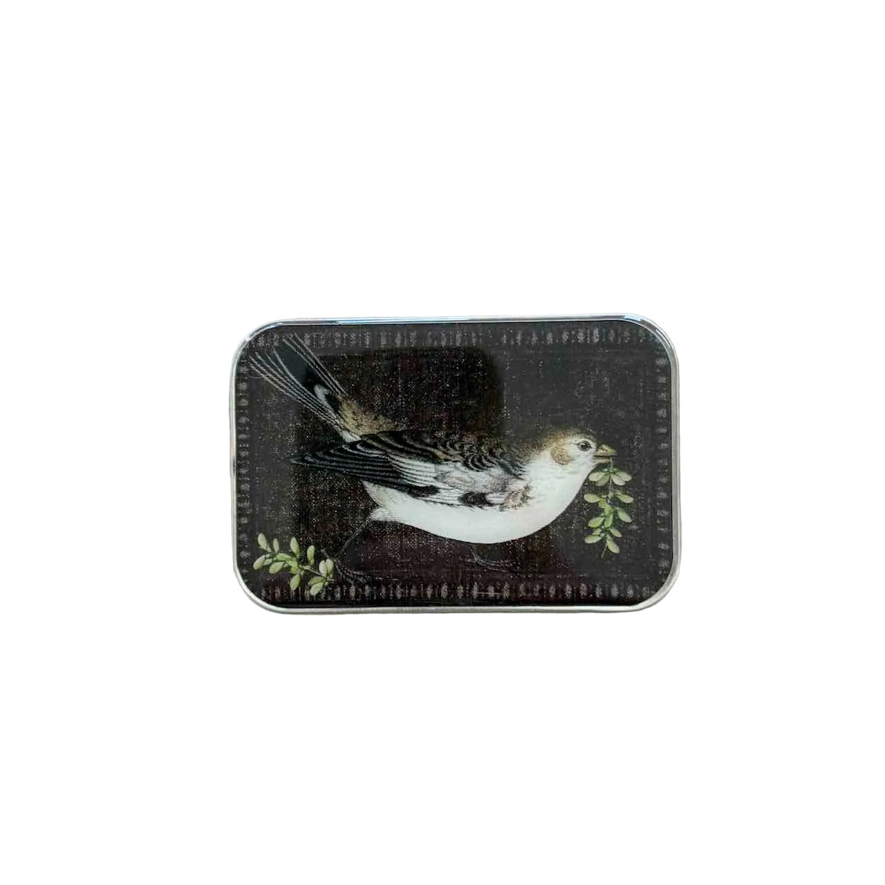 A rectangular tin with rounded corners featuring an illustration of a small white bird with black and brown markings holding green leaves, placed on a light wood surface.