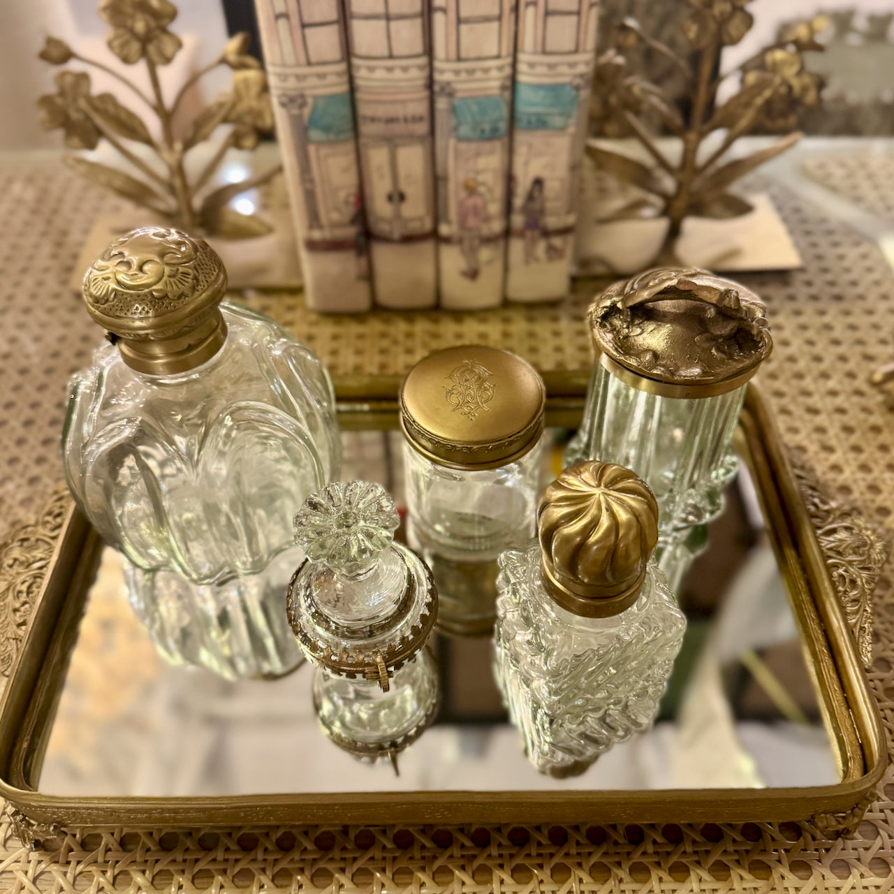 Set of decorative glass bottles with gold lids on a mirrored tray.