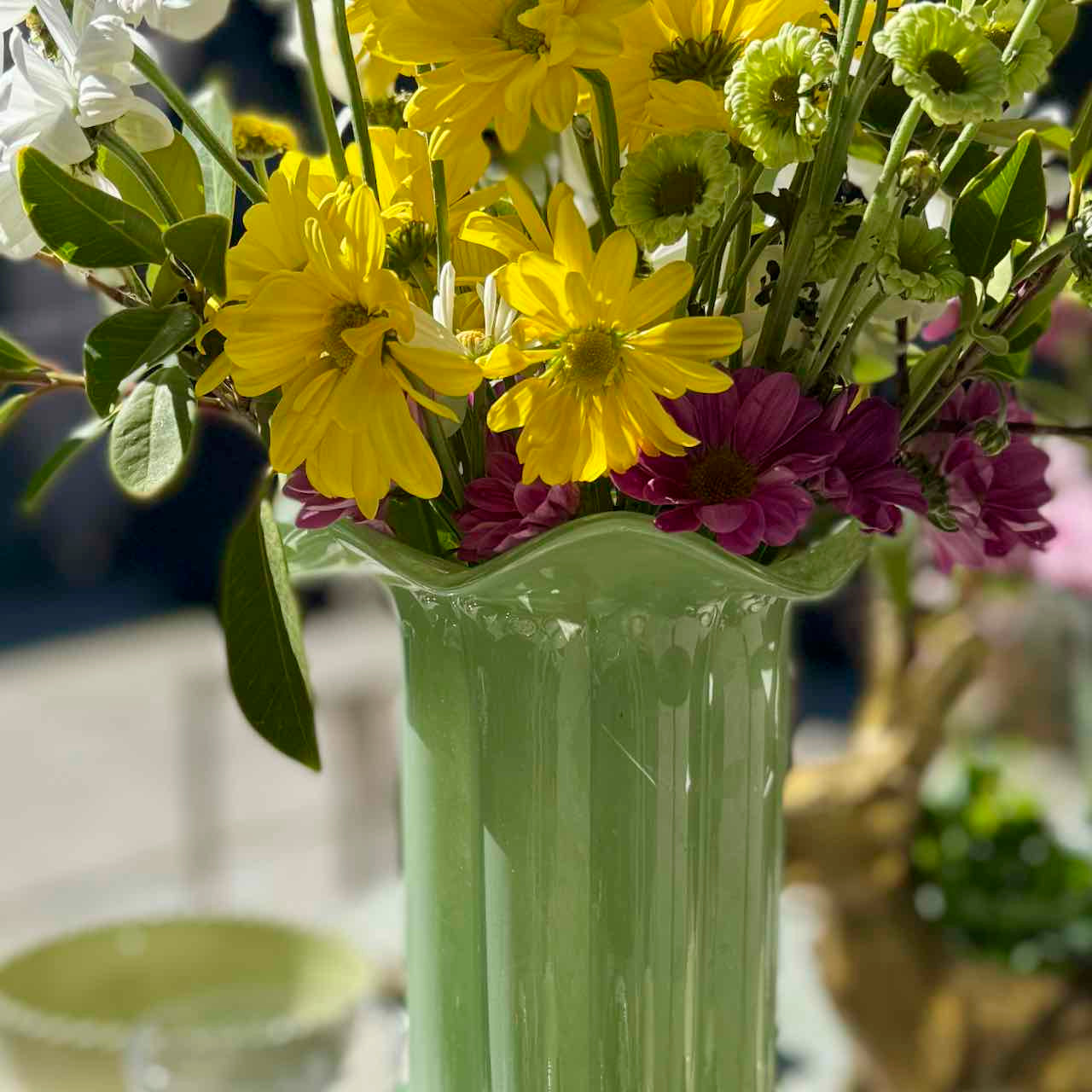 Green vase with yellow and purple flowers on a blurred background