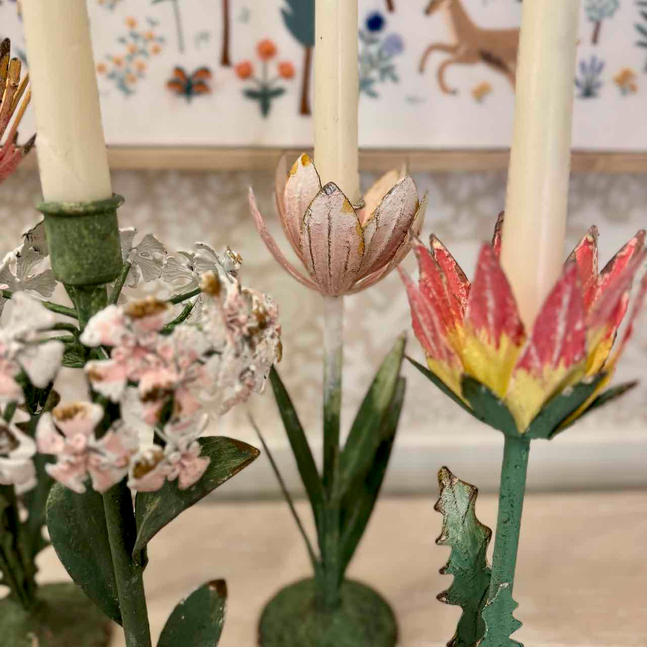 Decorative metal flower candle holders with candles against a floral-patterned background