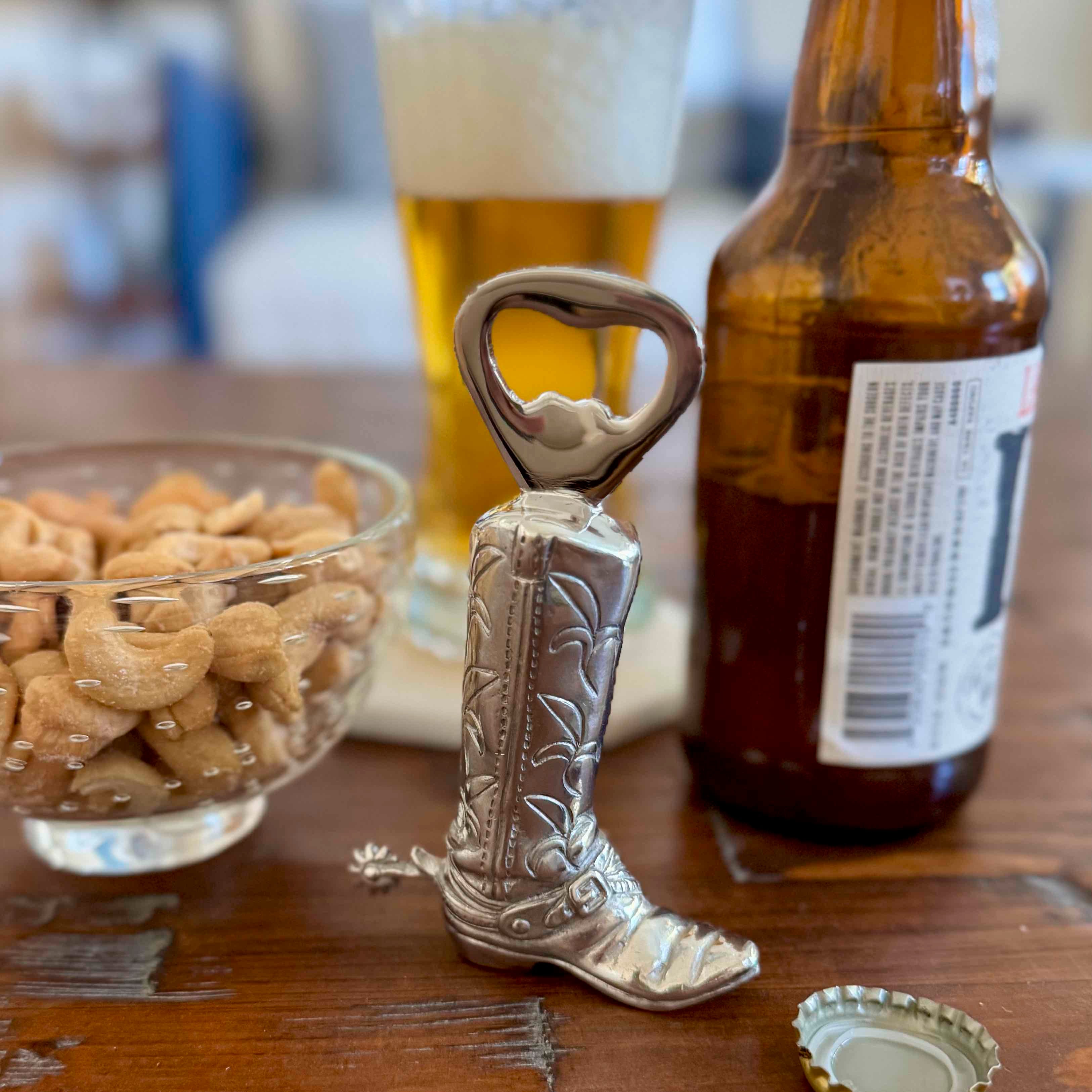 Cowboy boot bottle opener with a beer bottle and glass of beer in the background on a wooden table.