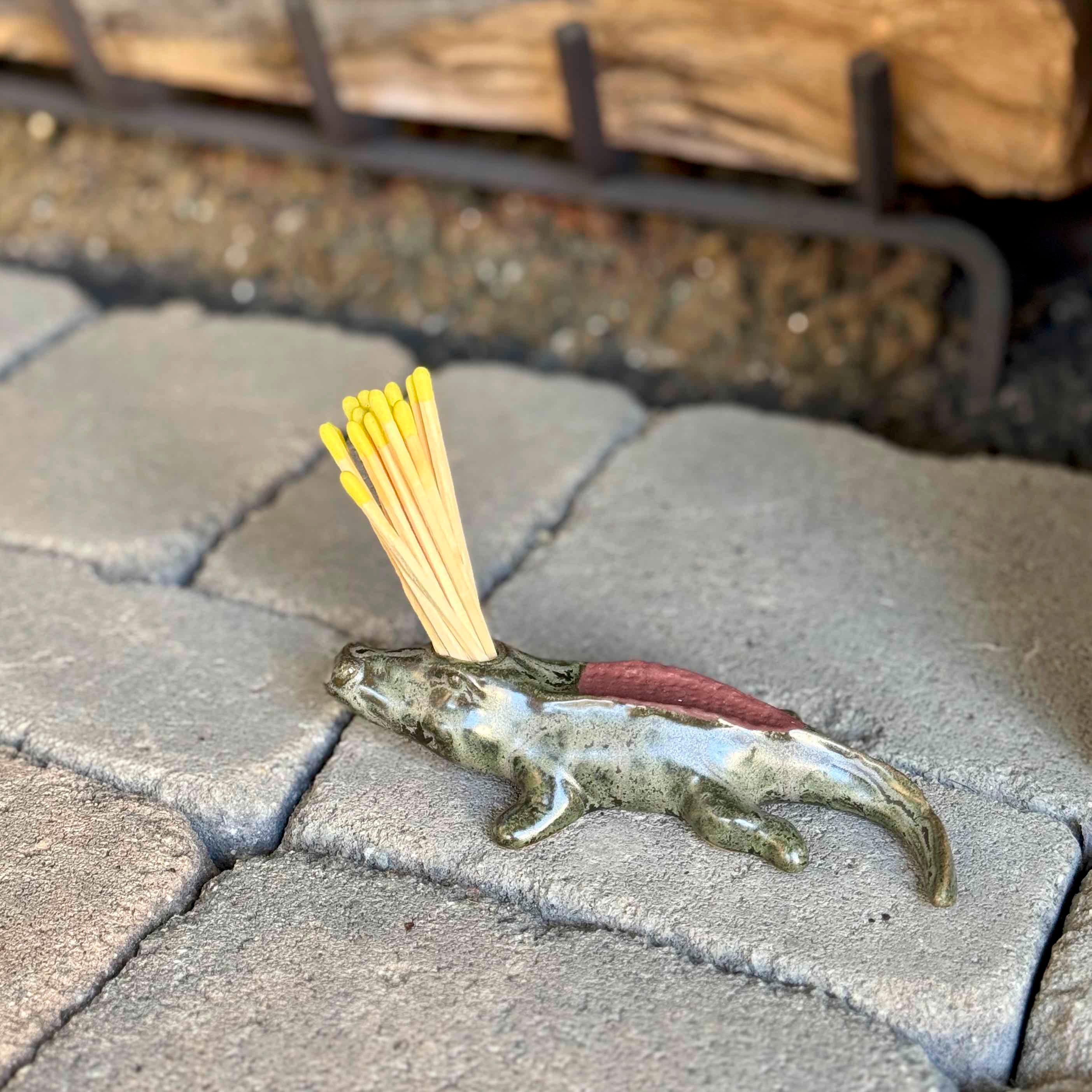 Small fish-shaped incense holder with yellow sticks on a stone surface