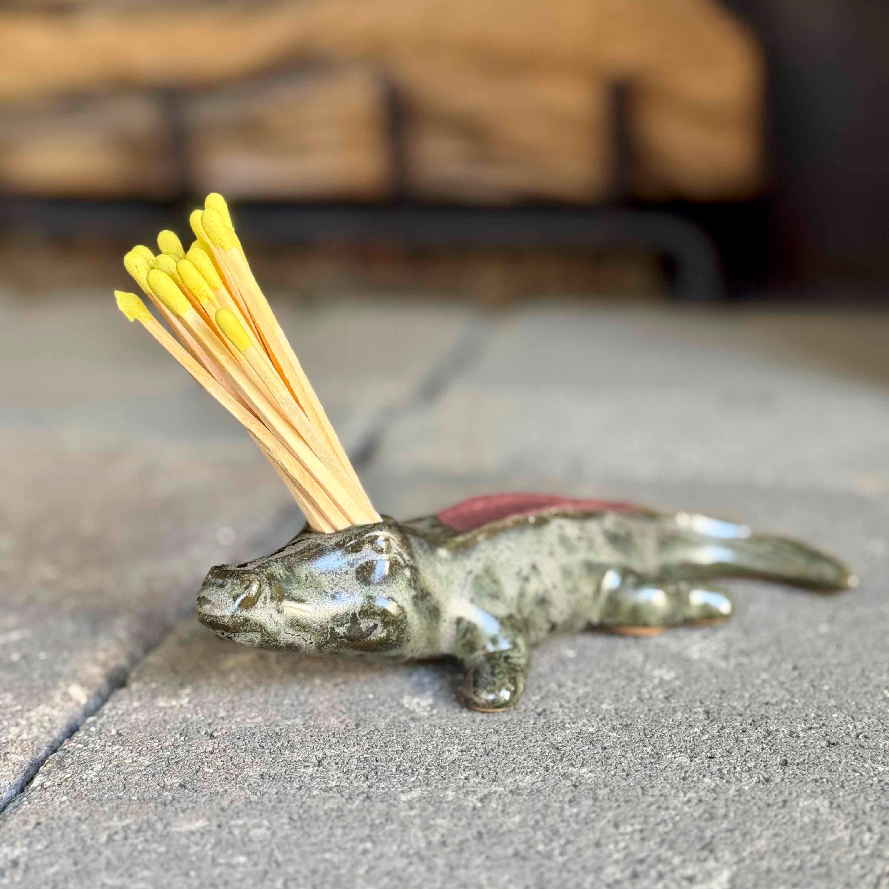 Lizard-shaped match holder with yellow matches on a concrete surface
