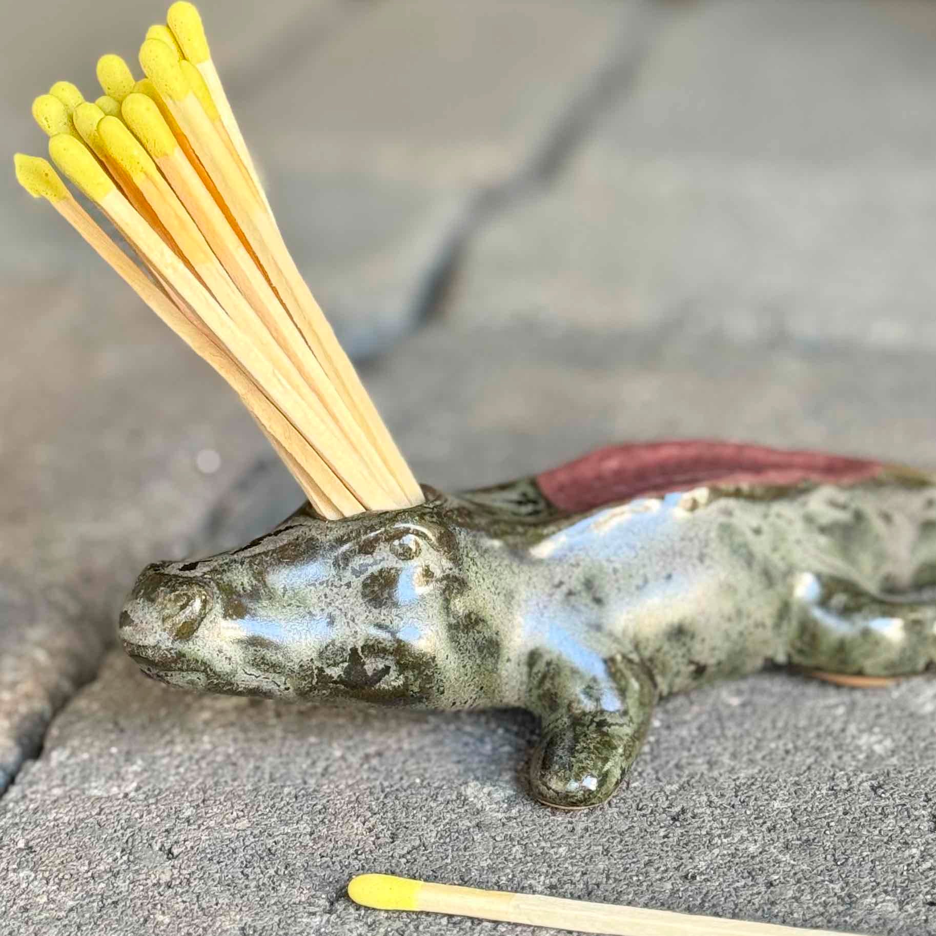 Matchstick holder shaped like a lizard with matches on a concrete surface