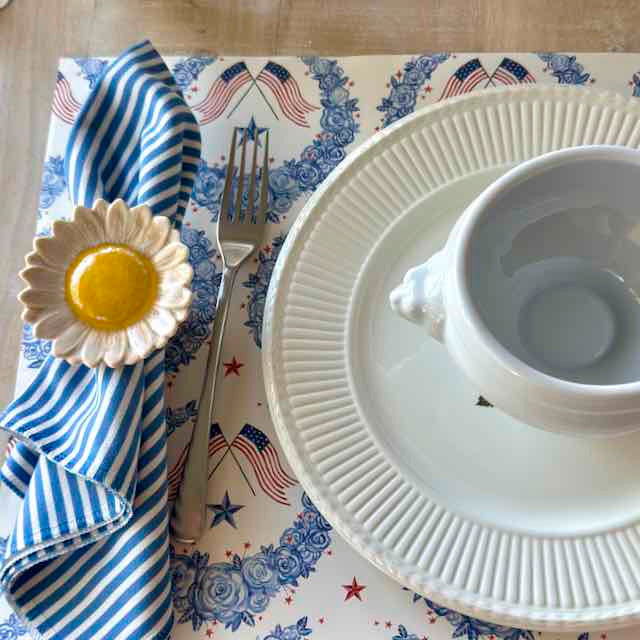 Dinner setting with white plates, a cup, and a decorative napkin on a tablecloth with American flag patterns.