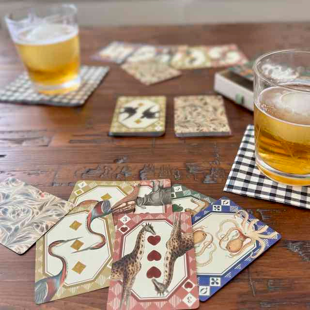 Playing cards with animal designs on a wooden table with glasses of beer.