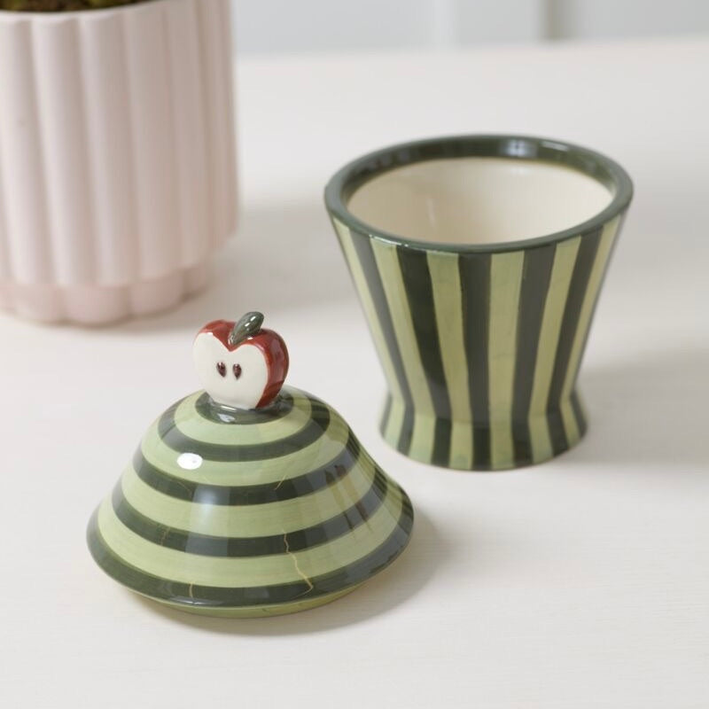 Ceramic container with striped design and apple-shaped knob on a white surface