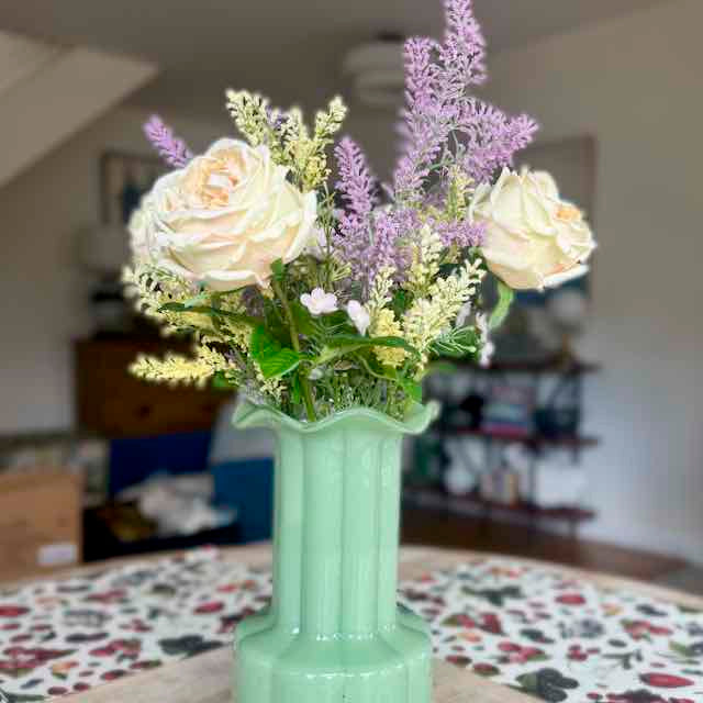 Bouquet of flowers in a green vase on a table with a blurred indoor background