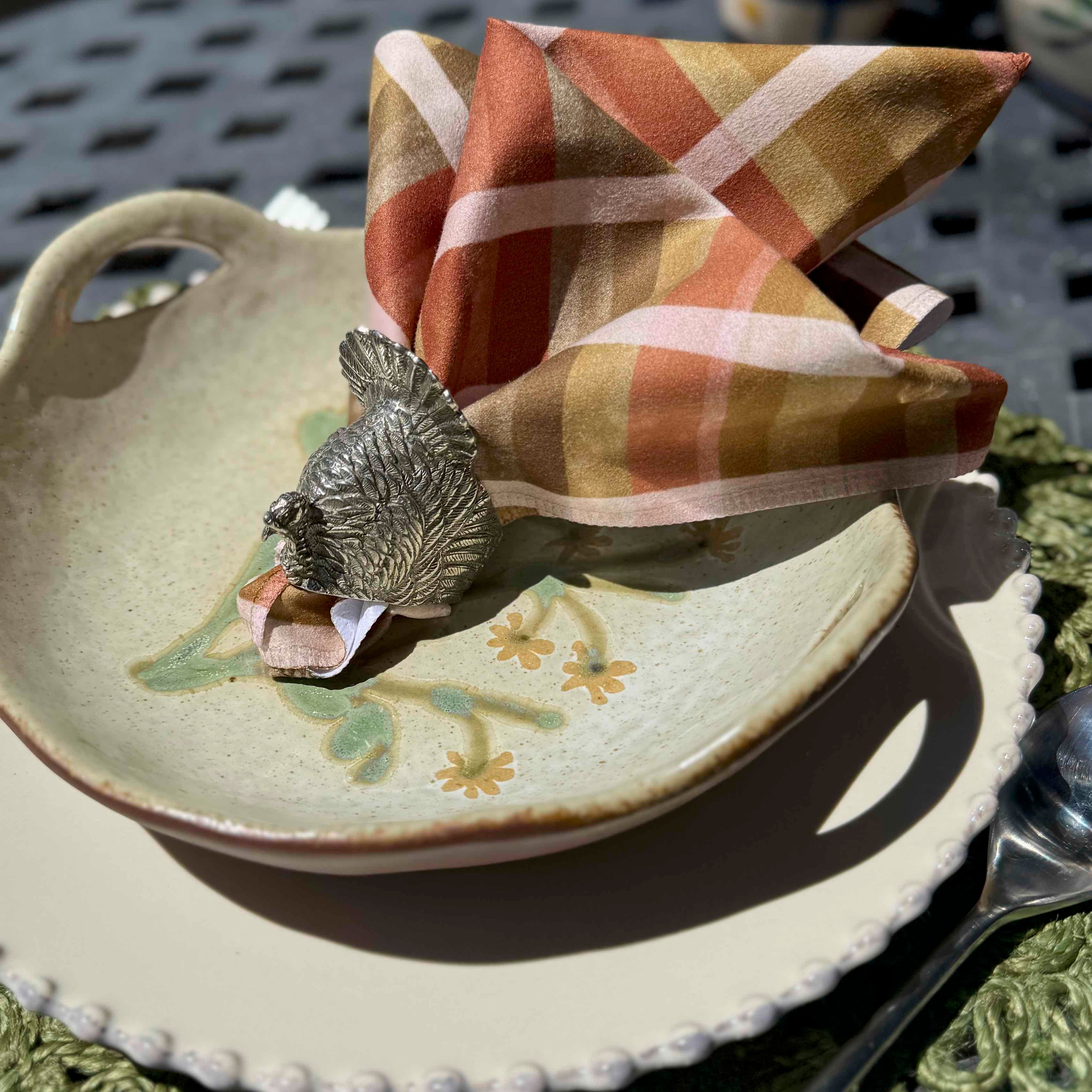 Decorative plate with a bird-shaped napkin holder and plaid napkin on a metal surface.