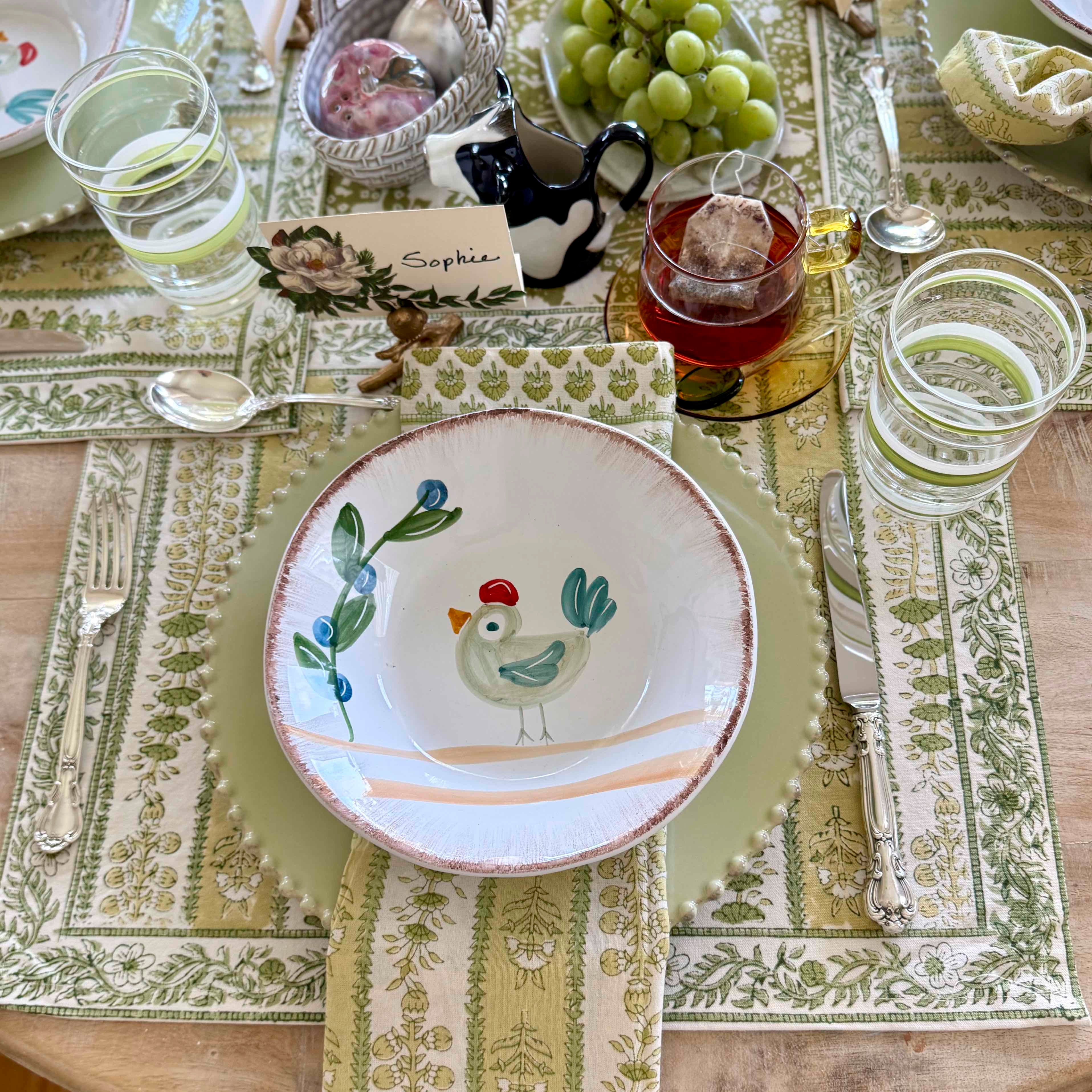 Dining table setting with a decorative plate featuring a chicken design on a patterned placemat.