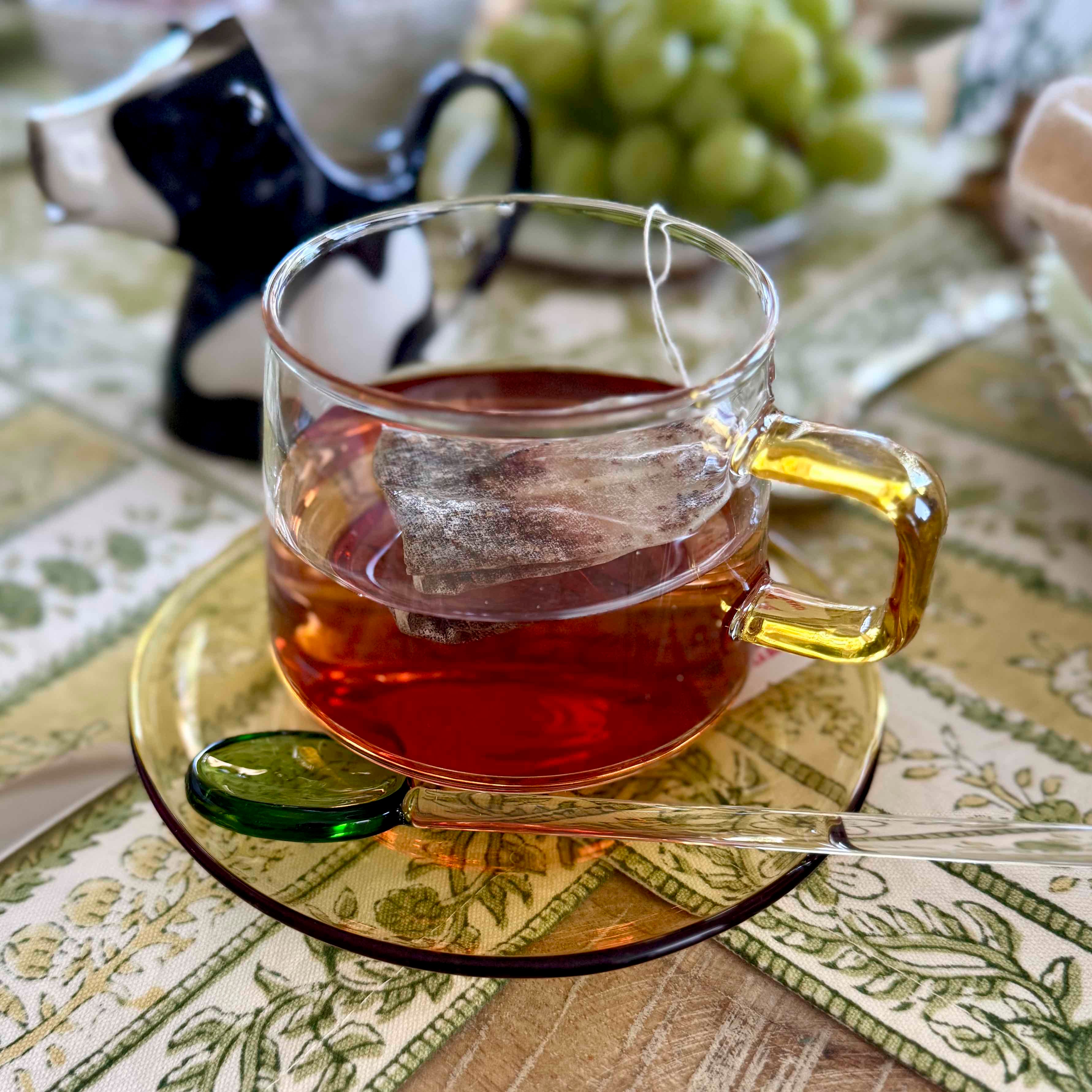 Clear glass mug with yellow handle filled with red tea, placed on a patterned tablecloth.