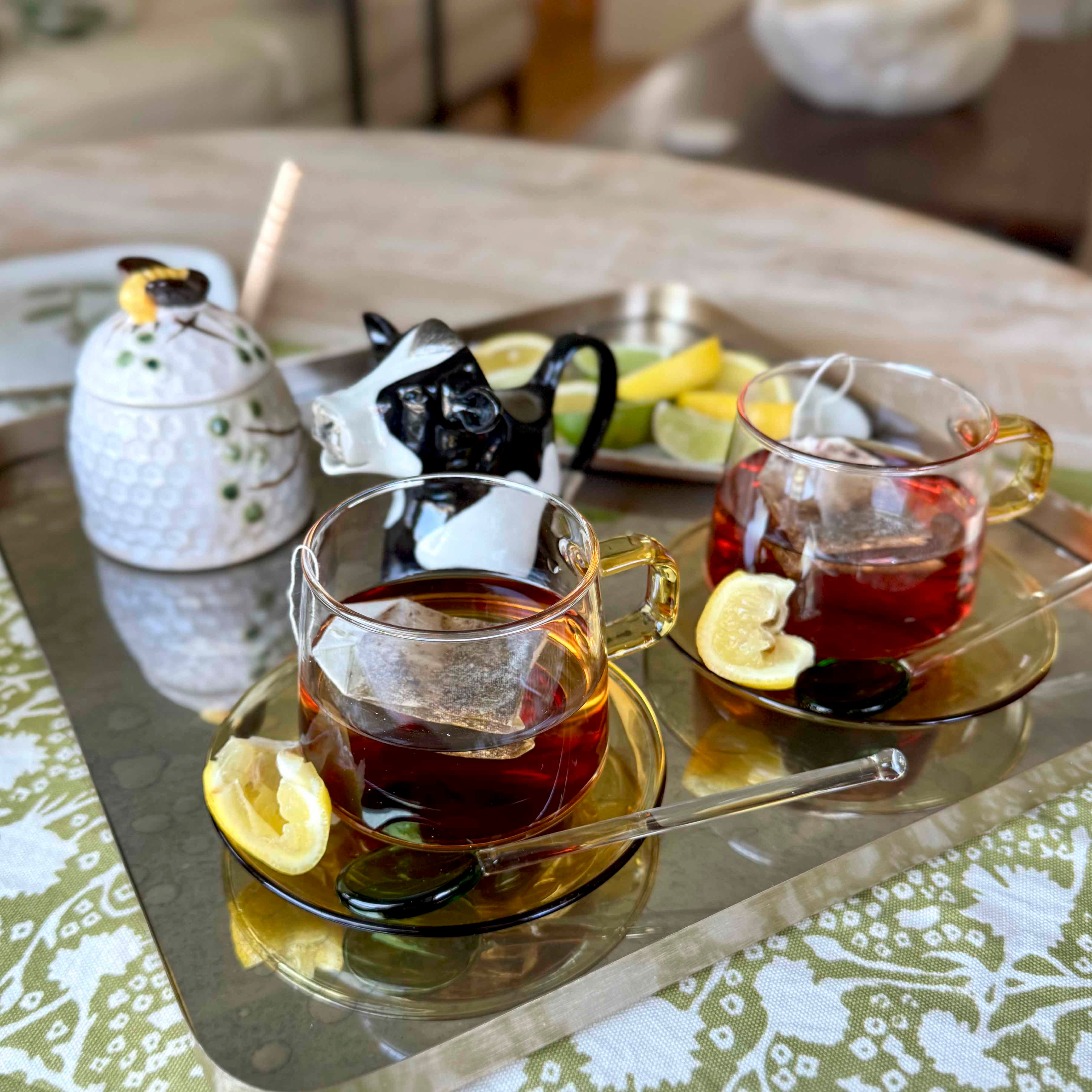 Tea-making setup with teapot, cups, lemon slices, and tea bags on a tray.