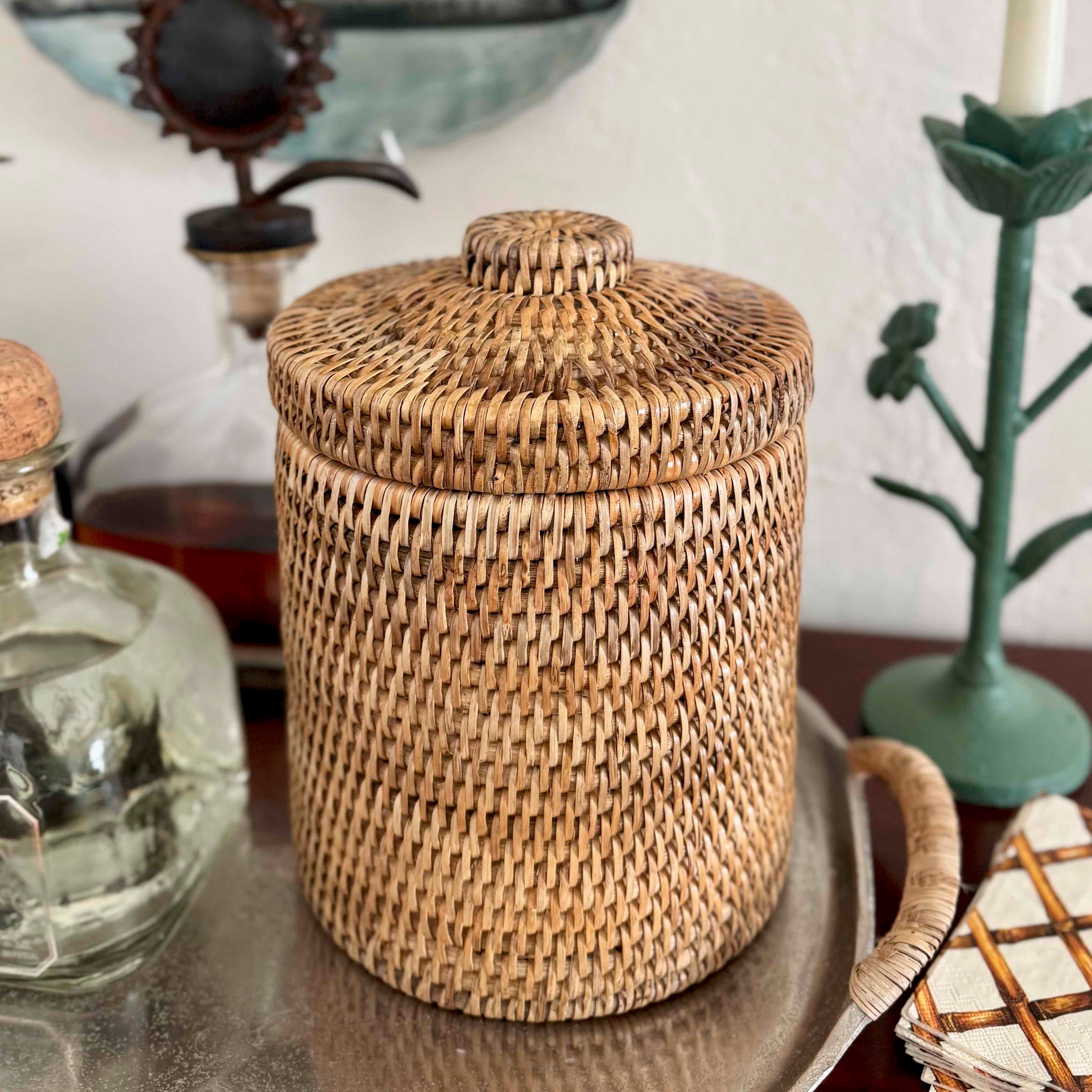 Woven rattan jar with a lid on a surface with decorative items in the background