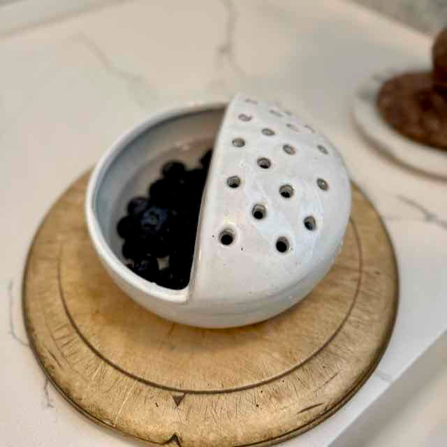 White ceramic tea ball with black tea leaves on a wooden coaster.
