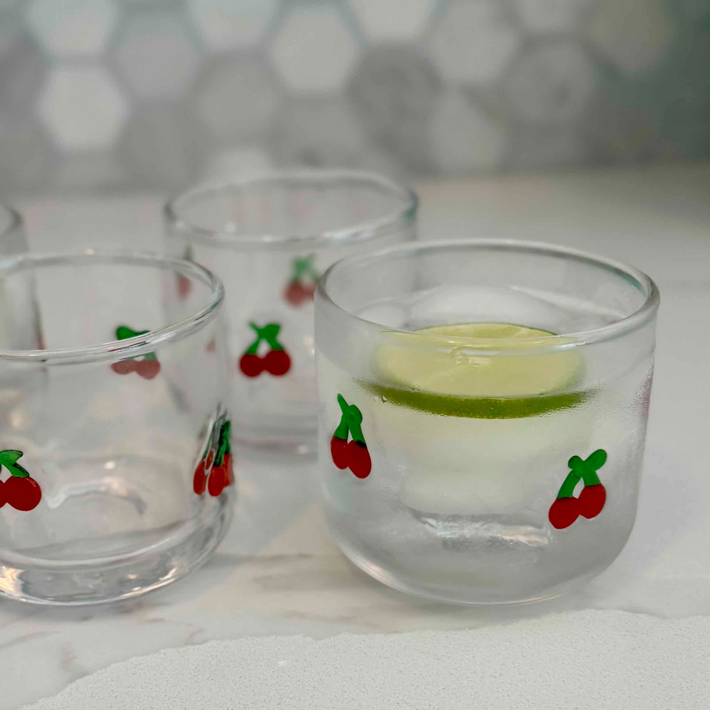 Three clear glasses with cherry designs on a white surface.