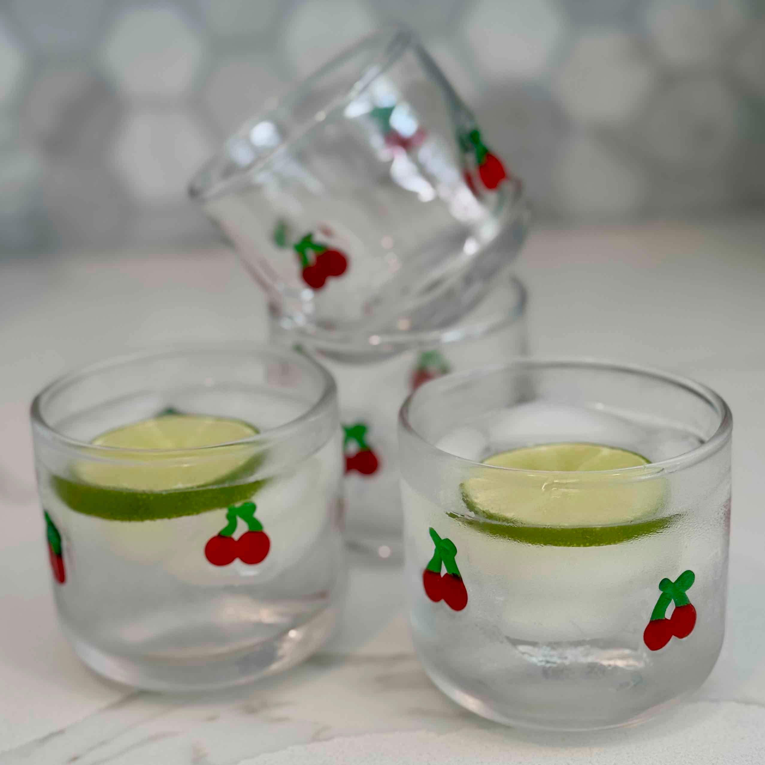 Three small glasses with lime slices and cherry decorations on a white surface.