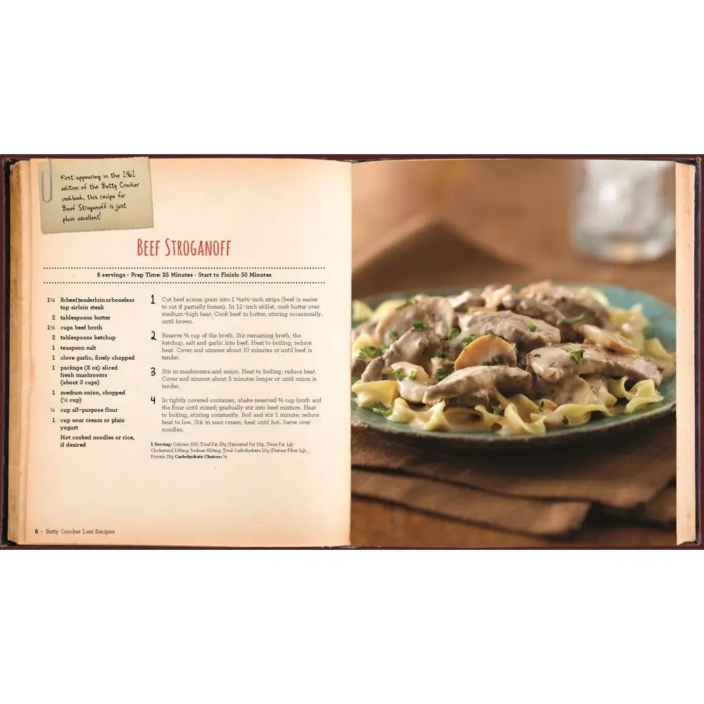 Open cookbook showing a recipe for Beef Stroganoff with a plate of food on a wooden table.