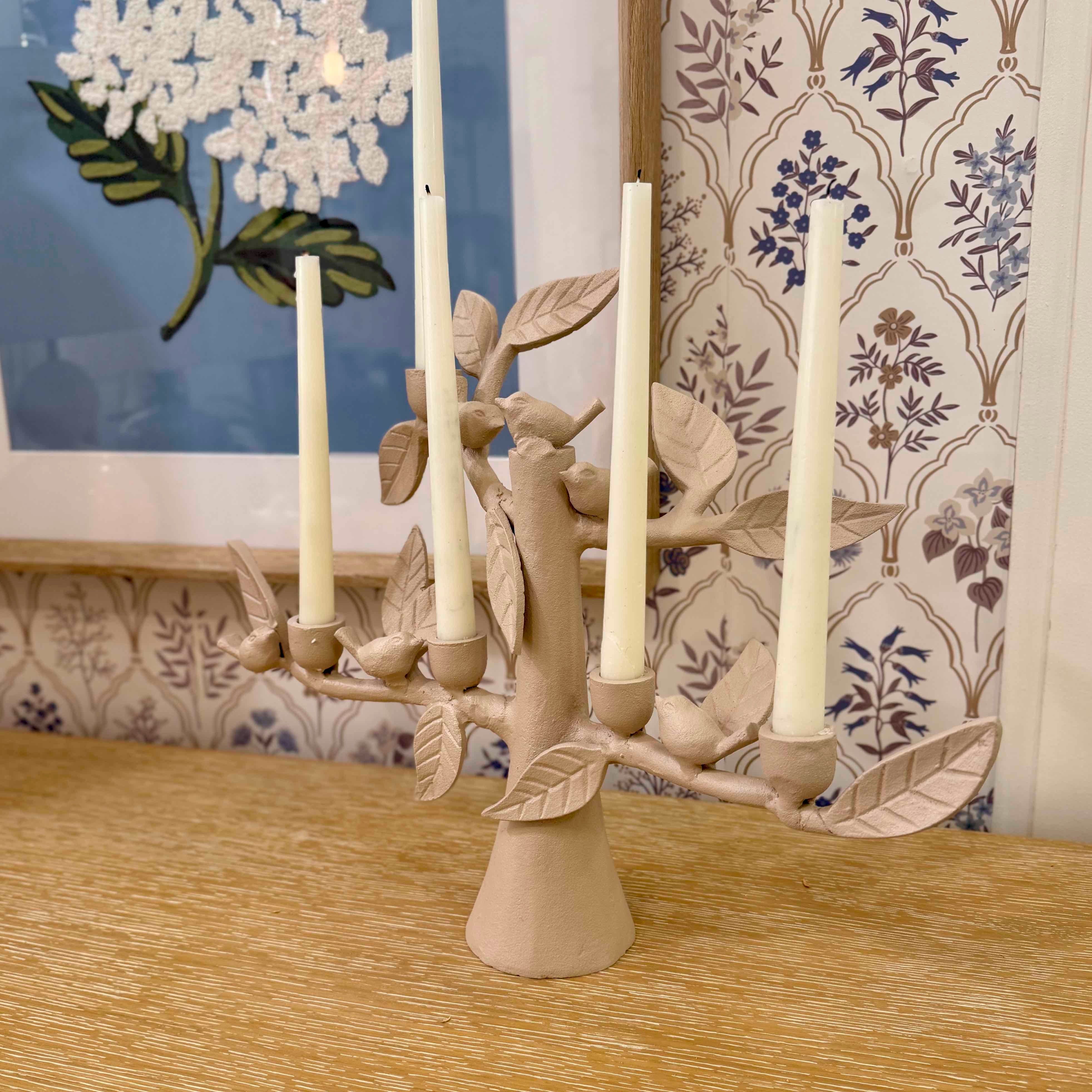 Decorative candle holder with leaves and birds on a wooden surface, floral wallpaper in the background