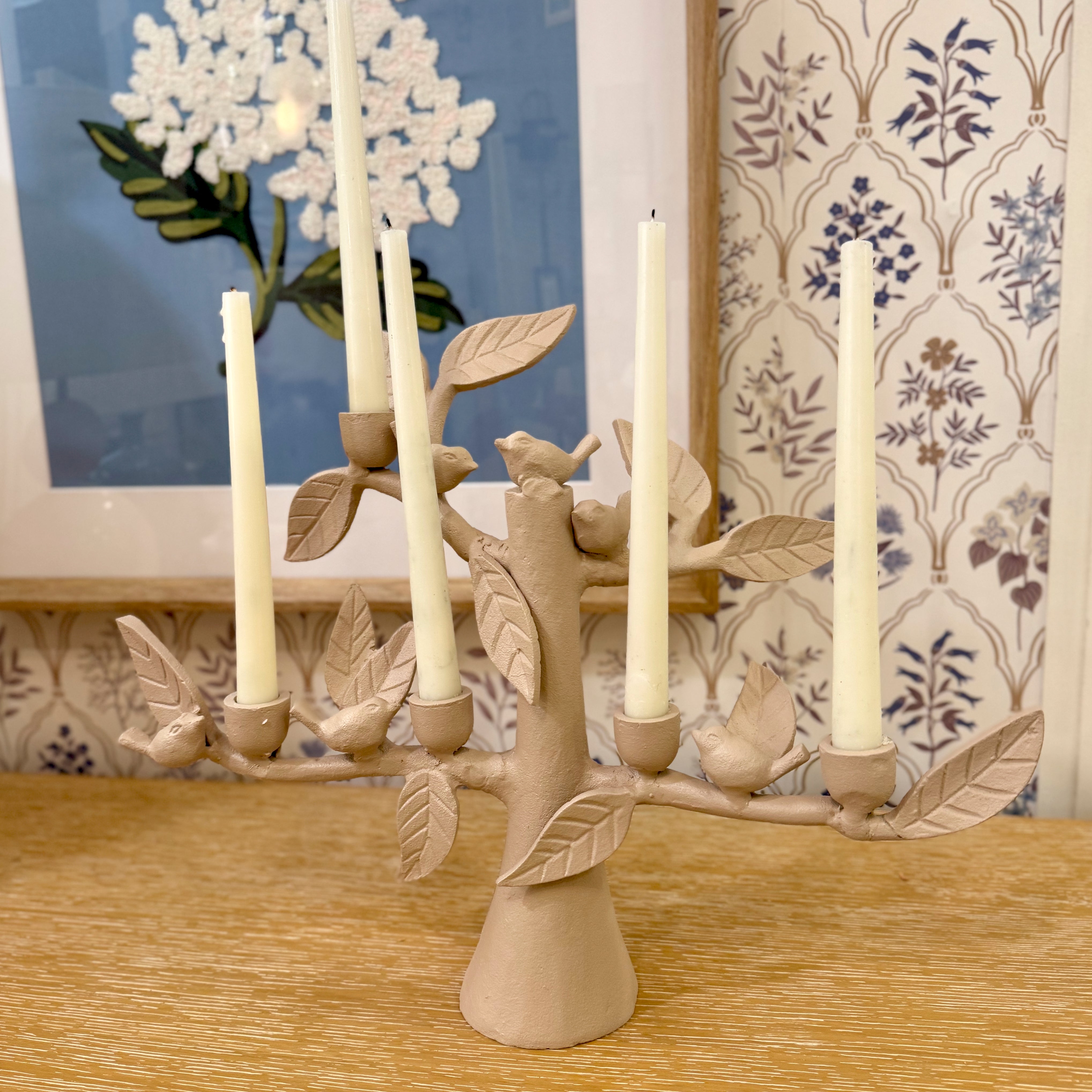 Ceramic candle holder with leaves and birds design on a wooden surface.