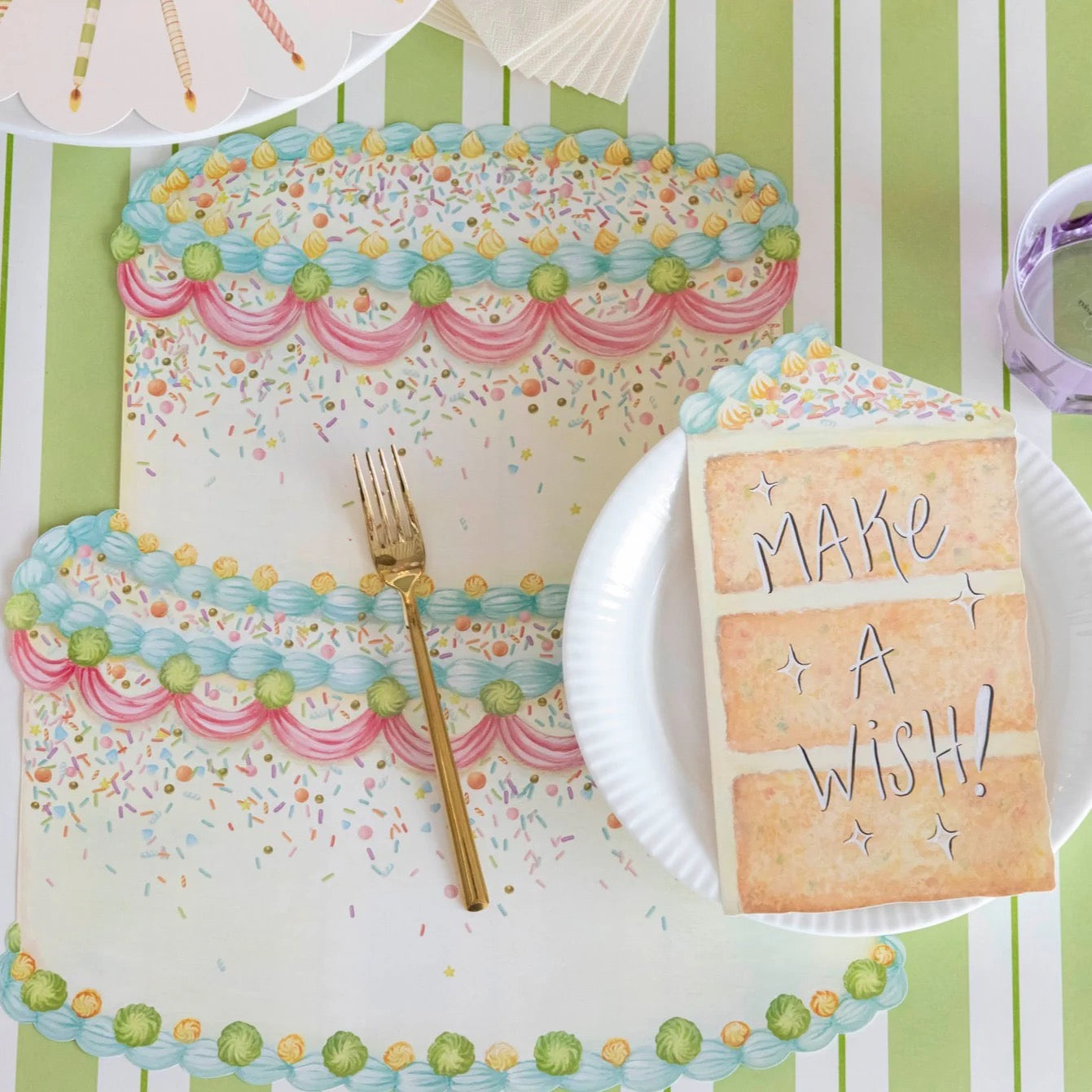 Decorative table setting with a cake, fork, and 'Make a Wish!' card on a green striped background.