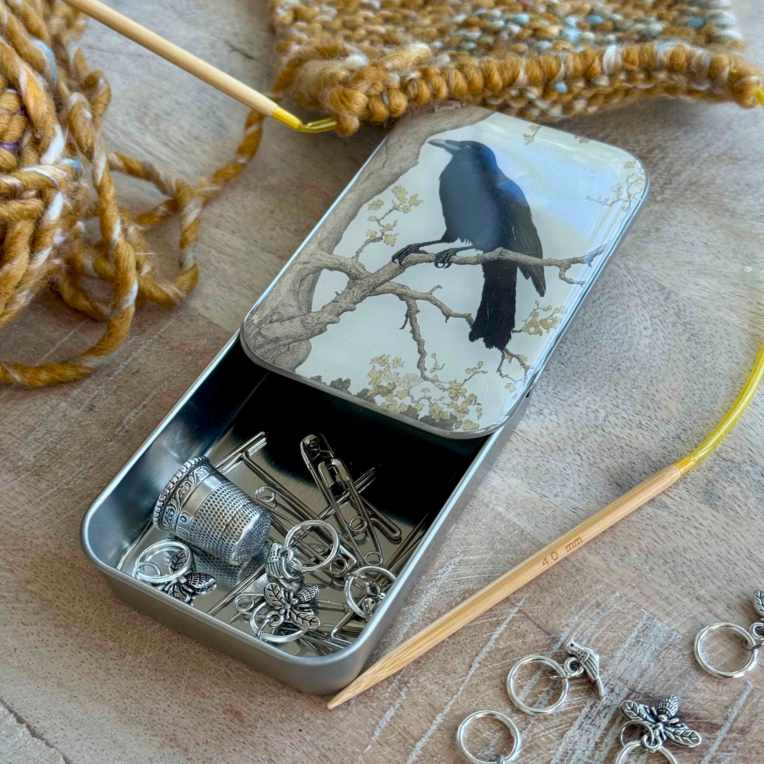Metal tin with jewelry-making supplies on a wooden surface