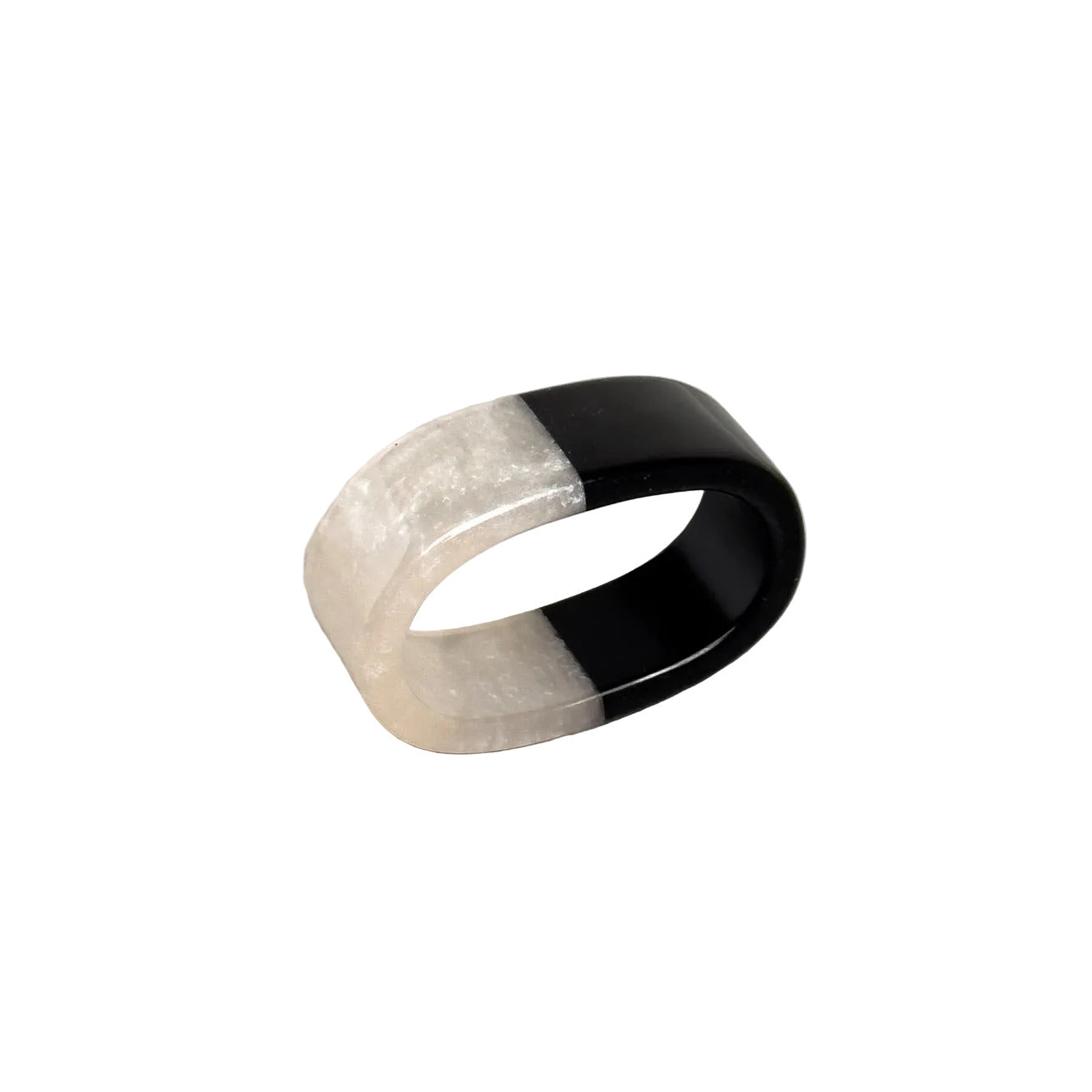 A wide band ring with a split design, featuring a textured translucent off-white outer half and a smooth glossy black inner half, resting on a gray textured surface.