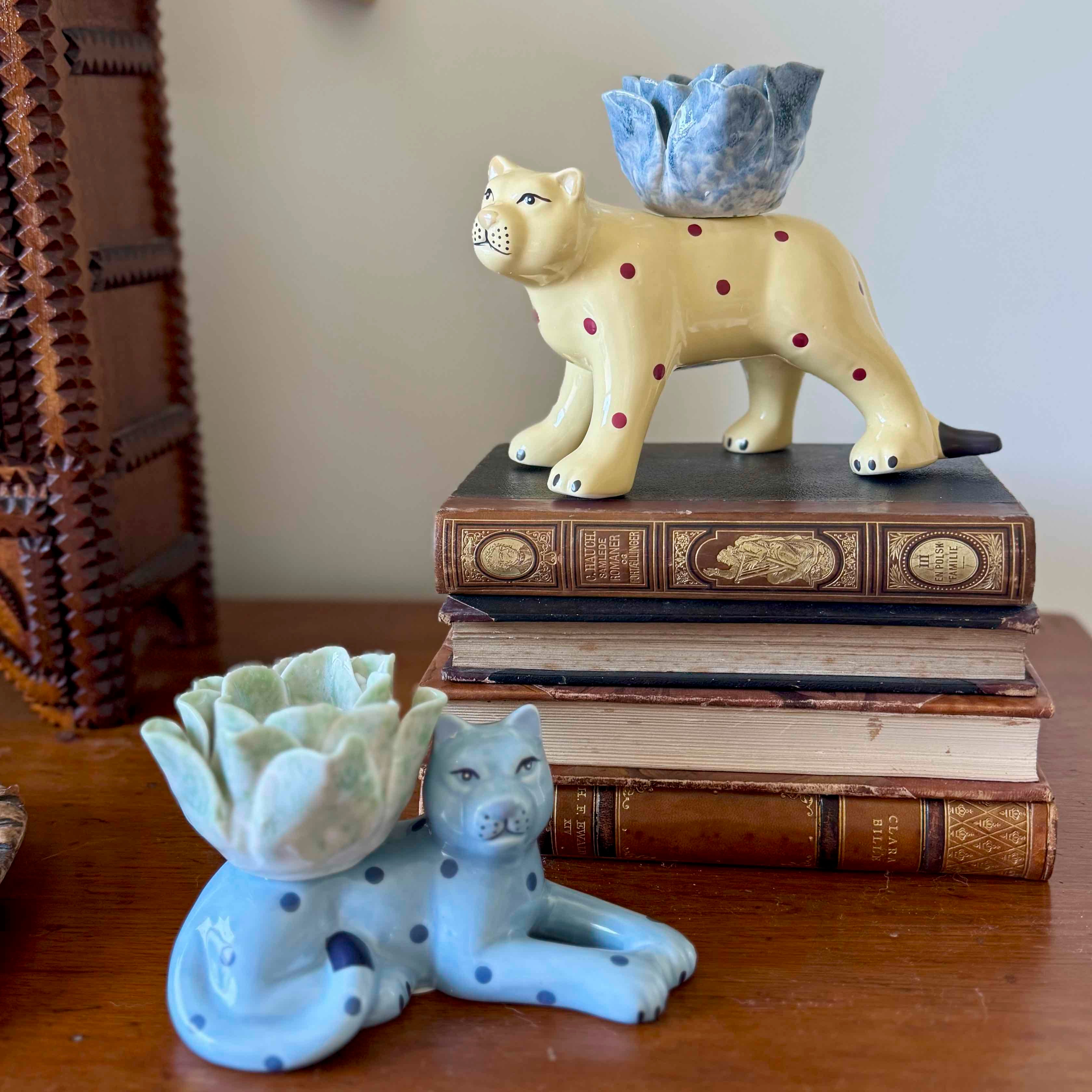 Two ceramic lion planters on a stack of books with a wooden shelf in the background.