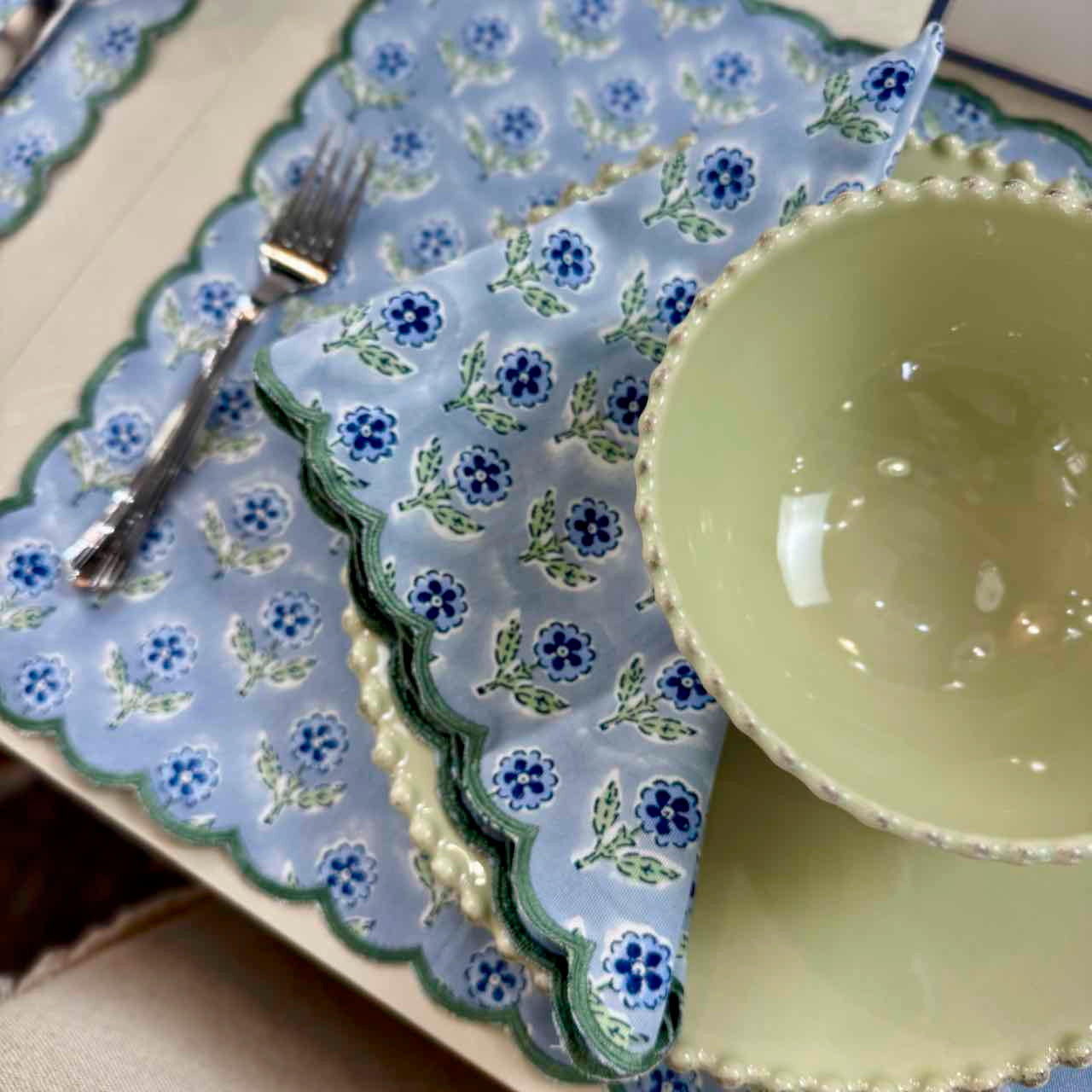 Set of green ceramic plates and bowls on a floral-patterned blue placemat.