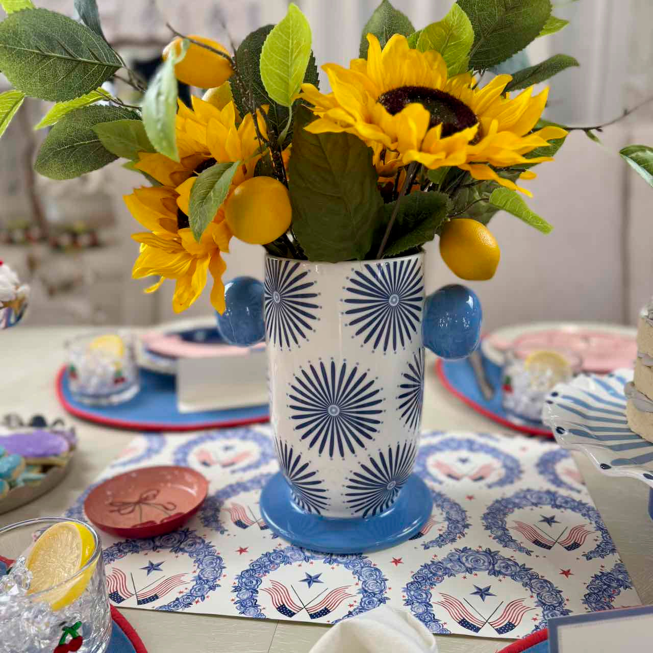 Decorative table setting with a vase of sunflowers and lemons on a patterned tablecloth.