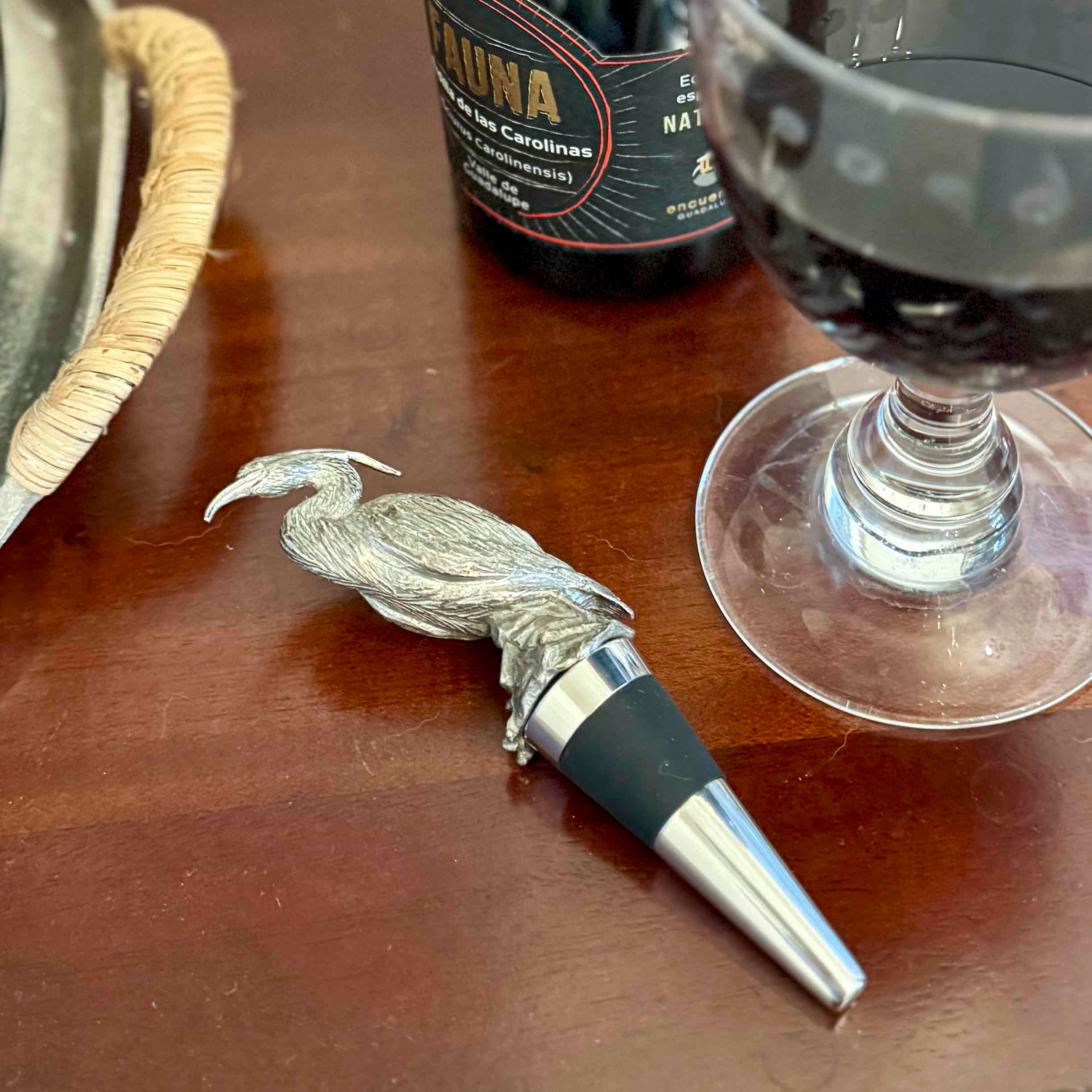 Wine bottle stopper with bird design on a wooden table with a wine glass and bottle in the background.