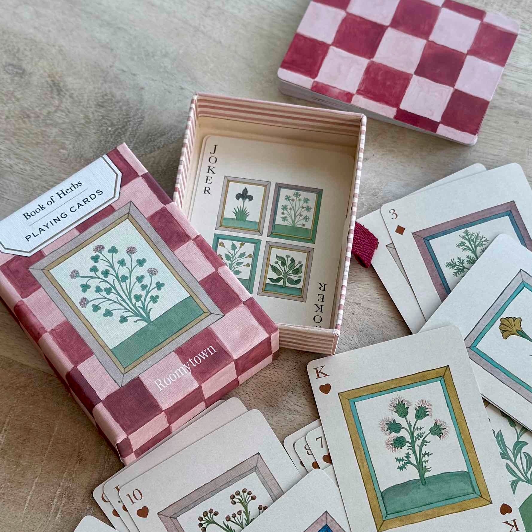 Playing cards with botanical designs and checkered box on a wooden surface
