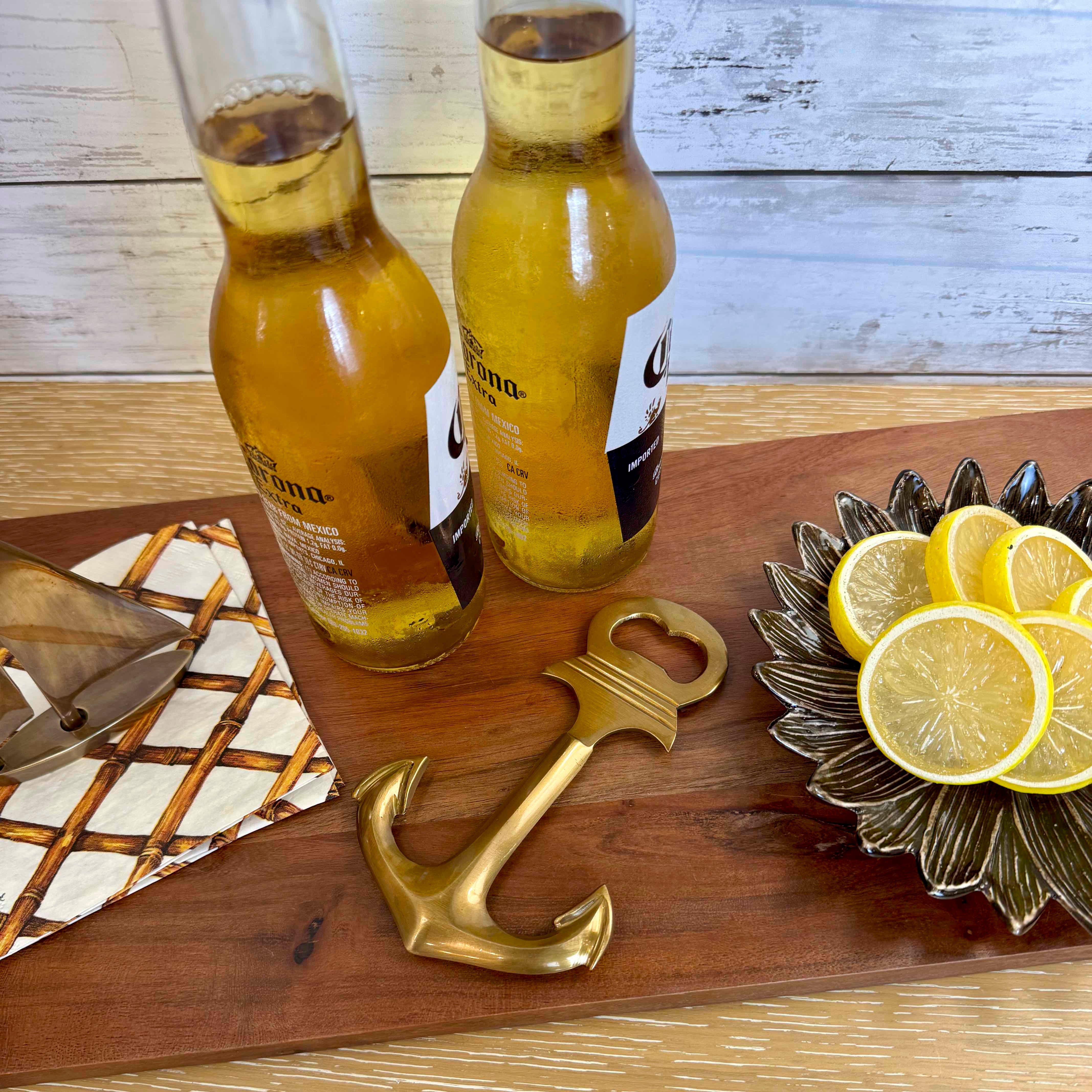 Two bottles of Corona beer on a wooden tray with a gold anchor bottle opener and lemon slices.