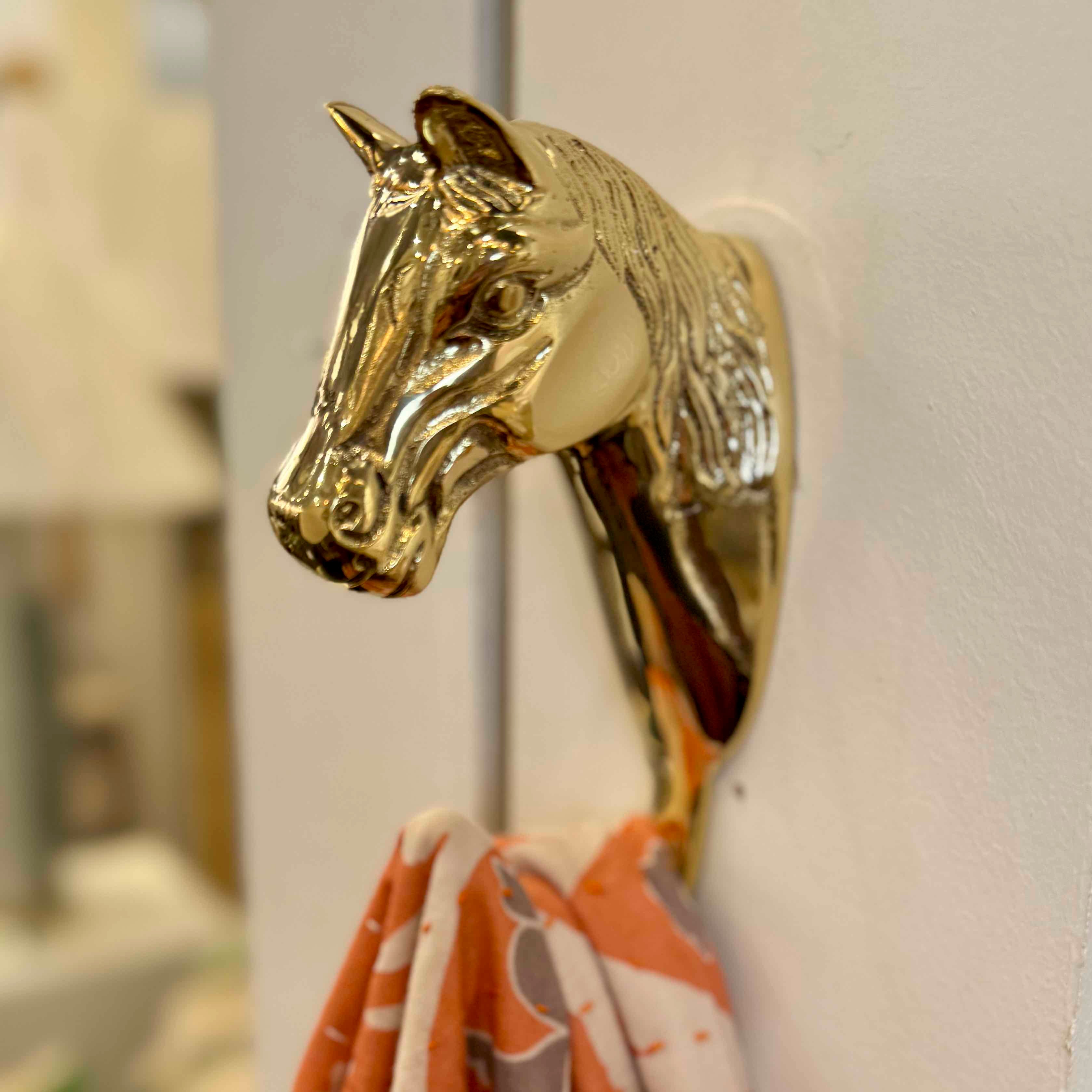 Gold horse head hook on a white wall with a towel hanging from it.