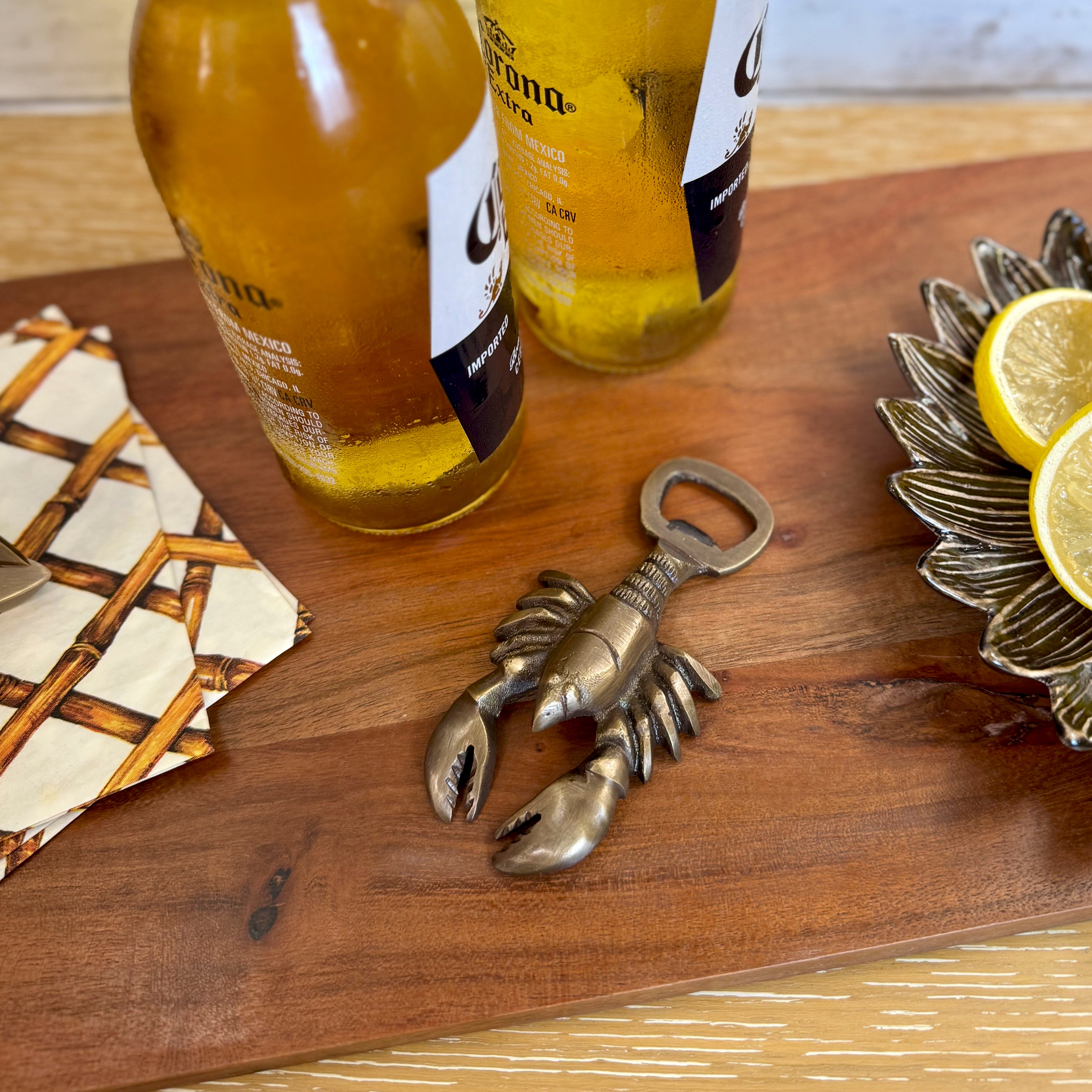 Two Corona beer bottles on a wooden surface with a lobster-shaped bottle opener and lemon slices.