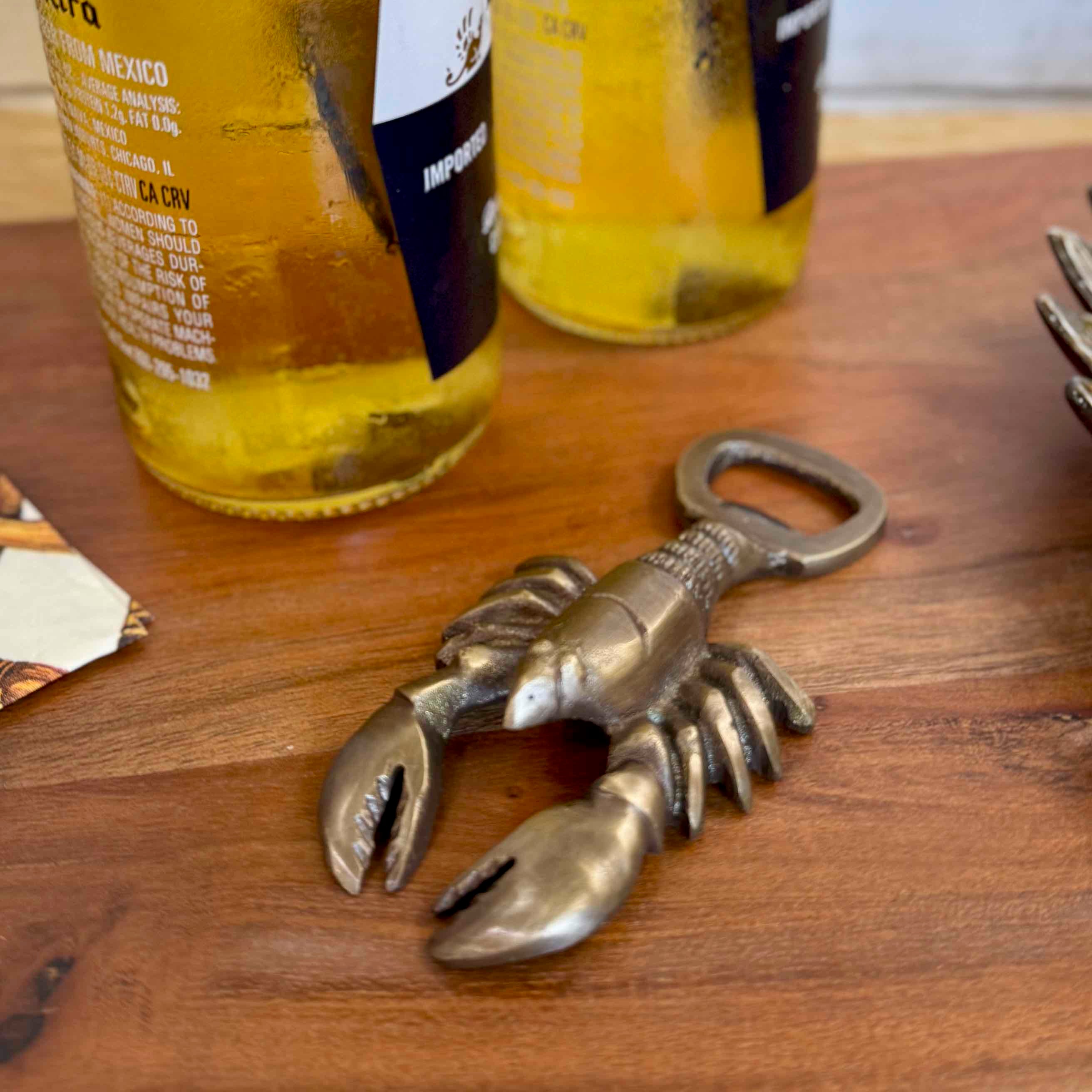 Brass lobster bottle opener on a wooden surface with beer bottles in the background