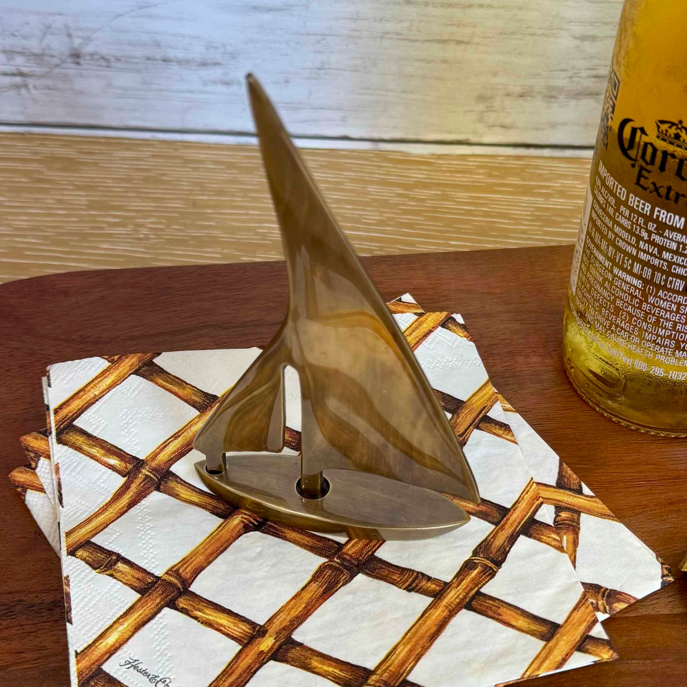 Decorative sailboat sculpture on a woven coaster with a beer bottle in the background.