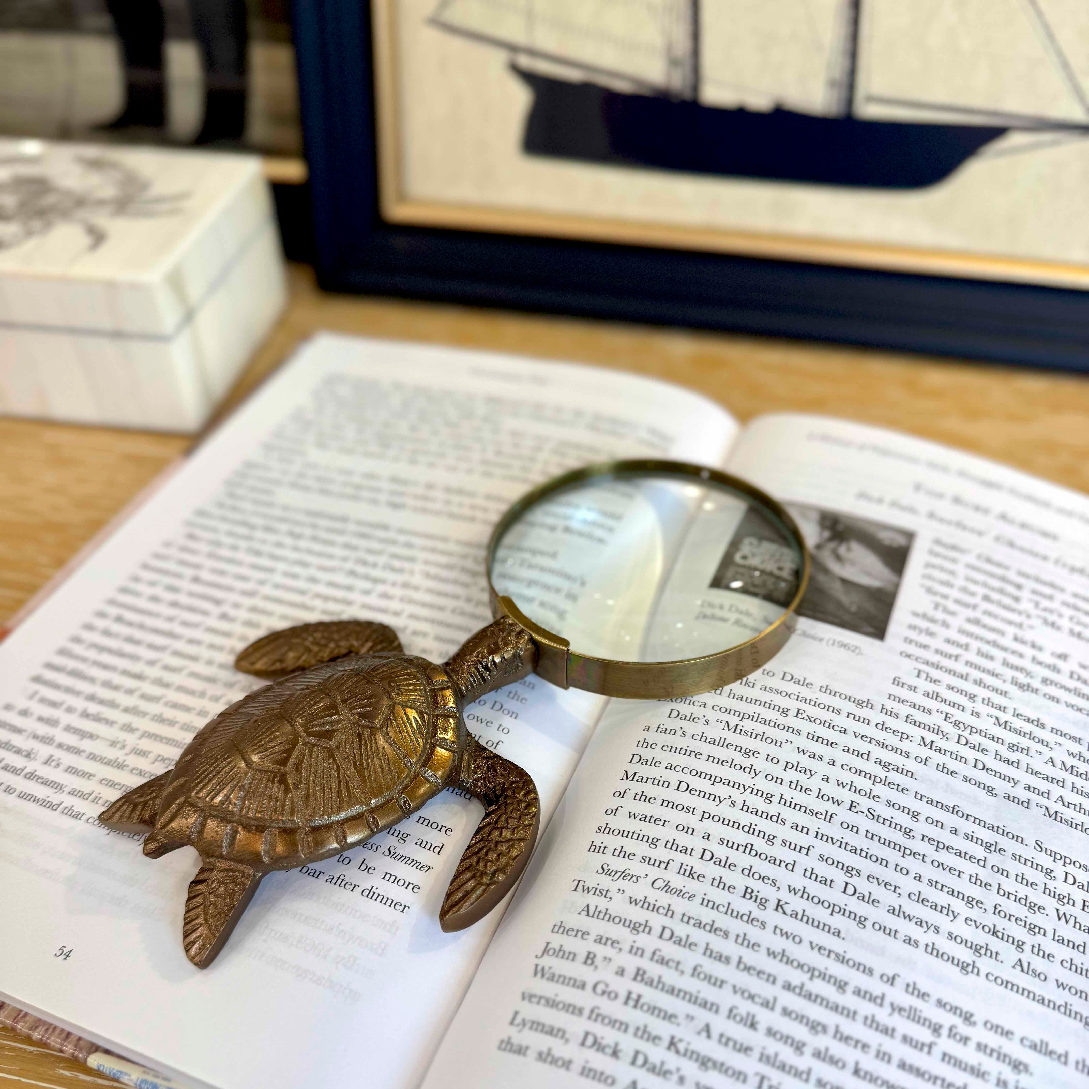 Brass turtle-shaped magnifying glass on an open book