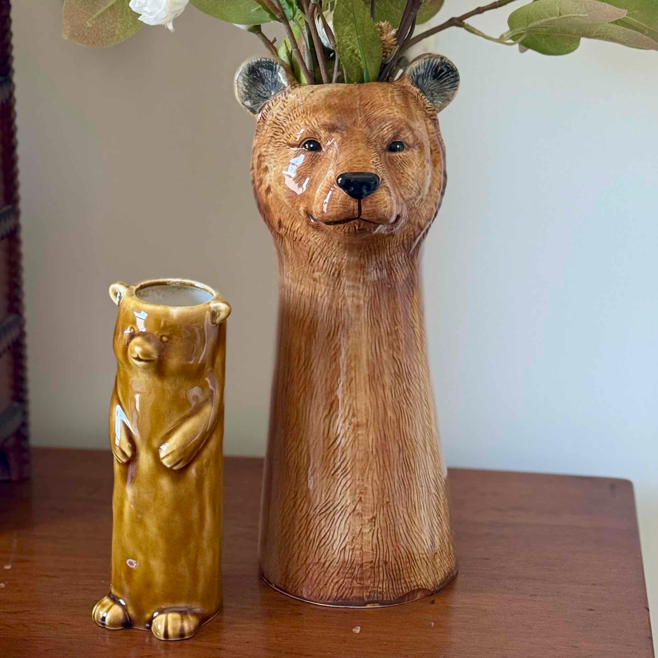 Two bear-shaped vases on a wooden surface with a plain background