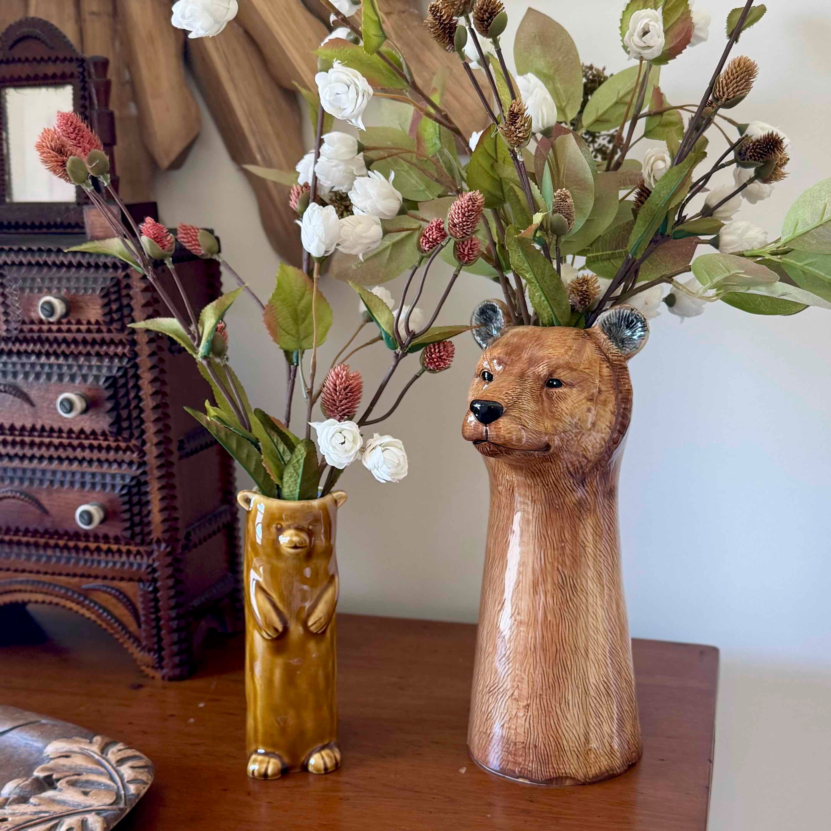 Two bear-shaped vases with floral arrangements on a wooden surface.