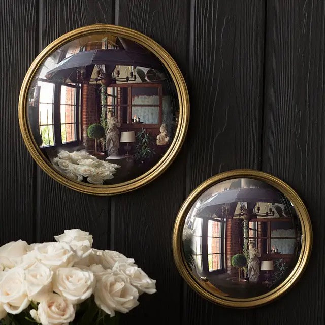 Two round gold-framed mirrors on a dark wooden wall with white roses in the foreground.