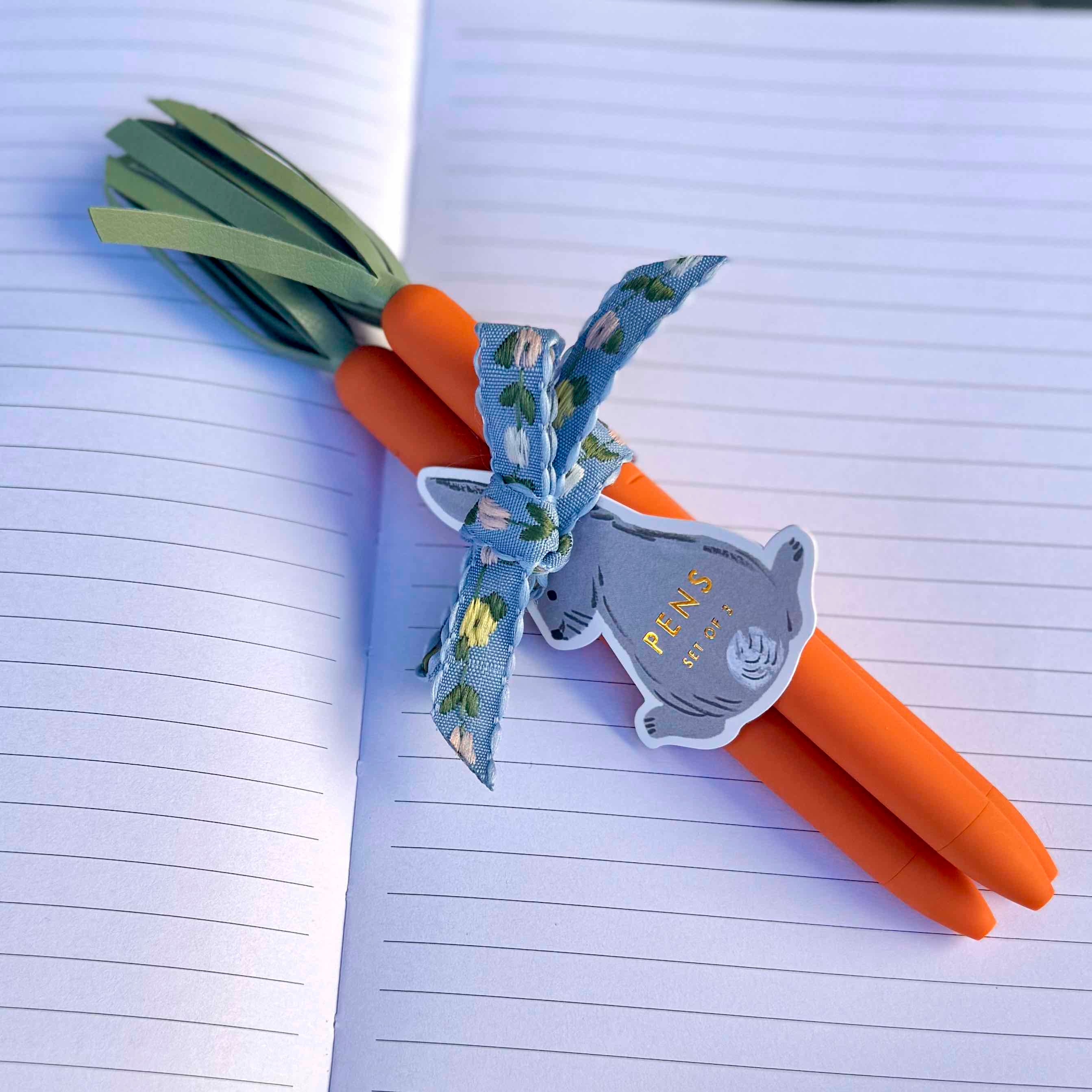 Carrot-shaped pen with a decorative bow on an open notebook