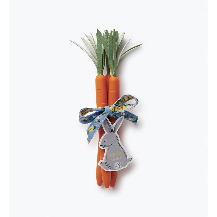 Three carrots with green tops tied together with a ribbon featuring a rabbit charm on a white background.