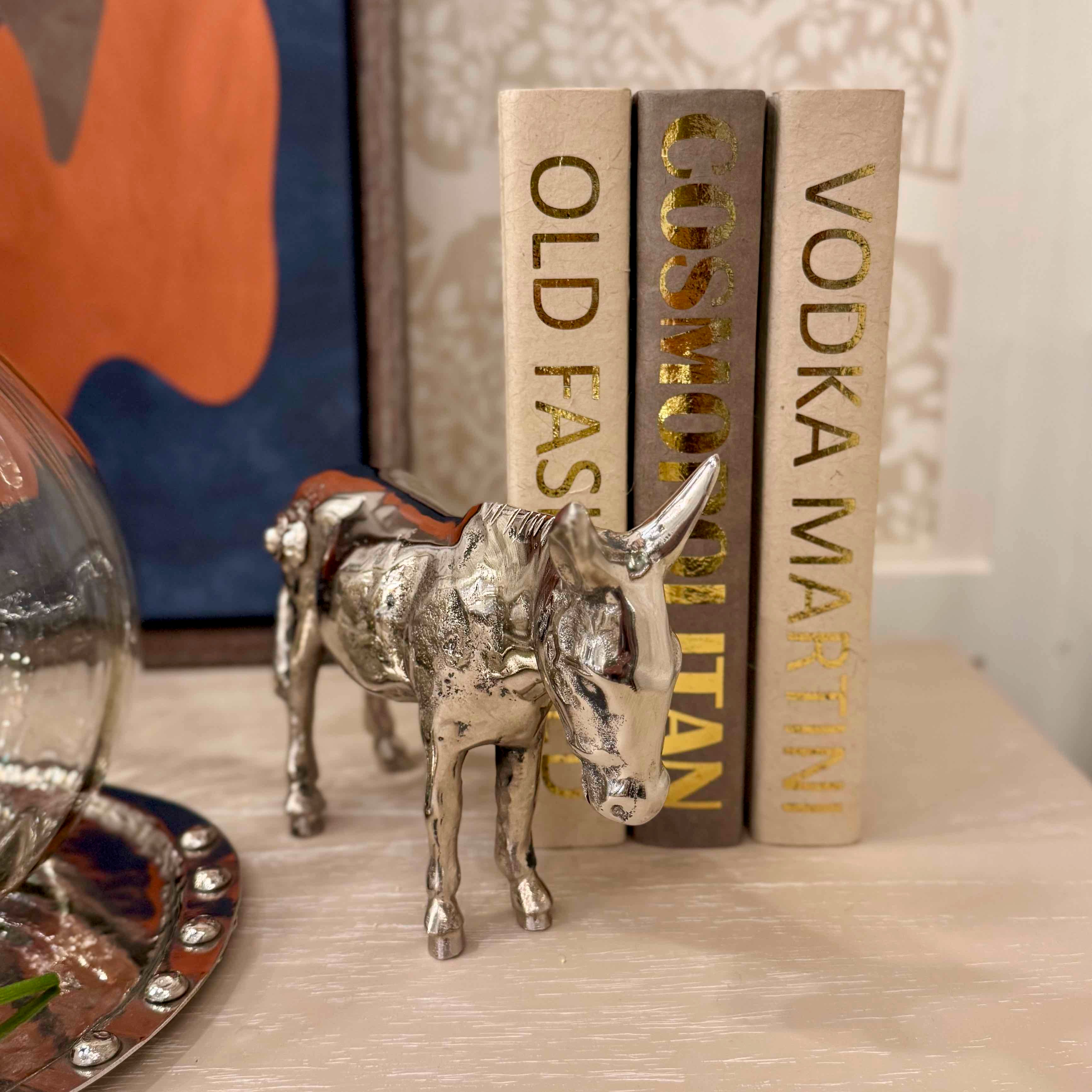 Silver donkey figurine on a surface with books in the background